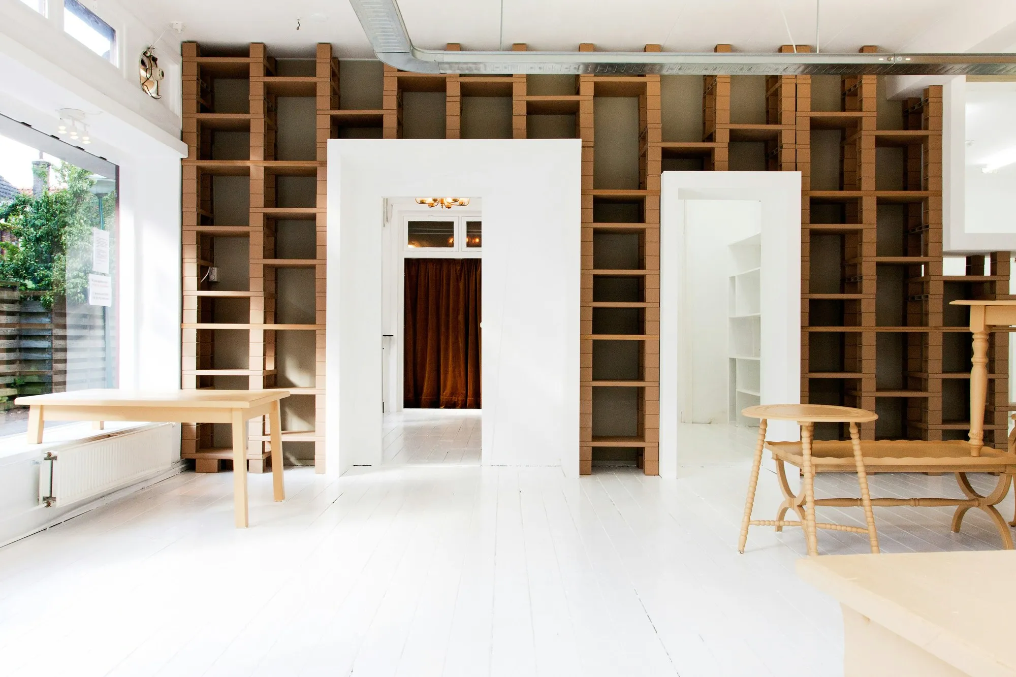 Bright studio interior with cardboard shelving, timber tables and white floor in soft daylight