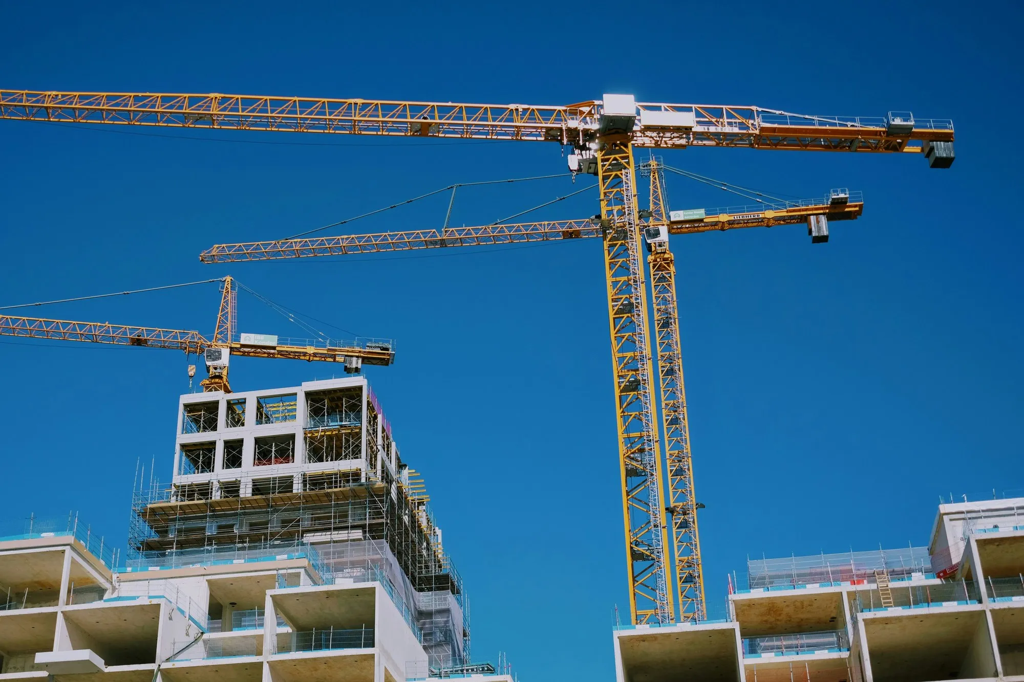 Tower cranes above a concrete-frame residential block under construction against a deep blue sky, Amsterdam