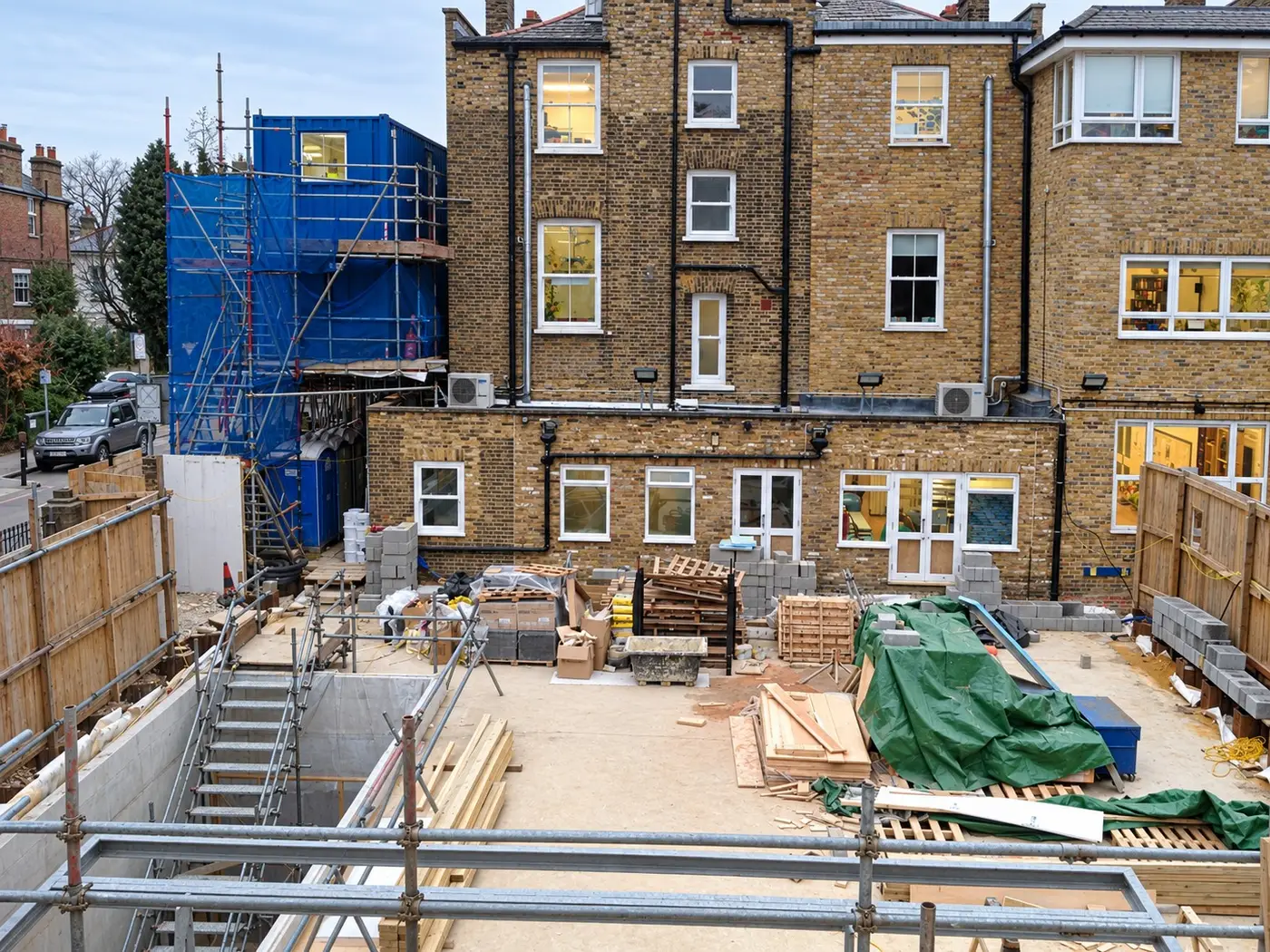 New-build ground slab behind a row of brick houses in London, with scaffold and materials on site