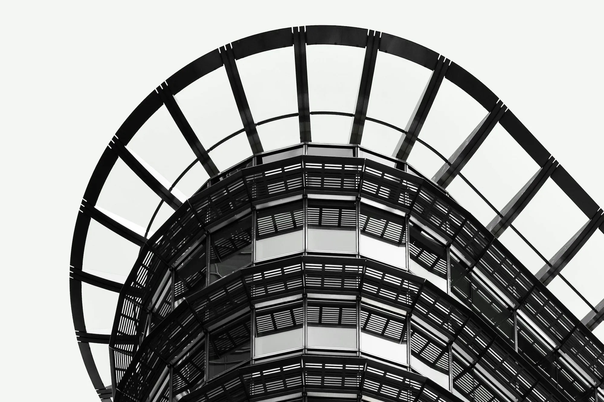 Curved black steel and glass office tower against a pale sky