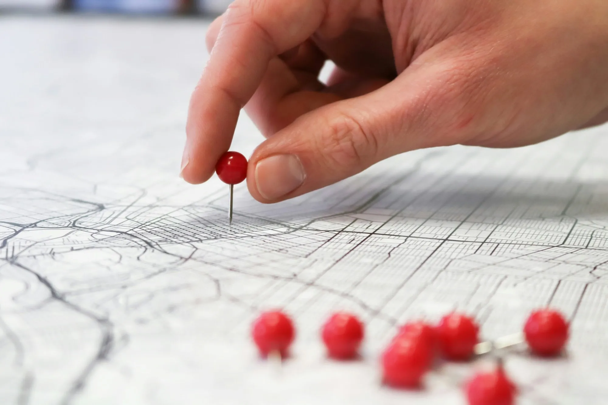 Hand placing a red pin on a printed city street map to mark a site