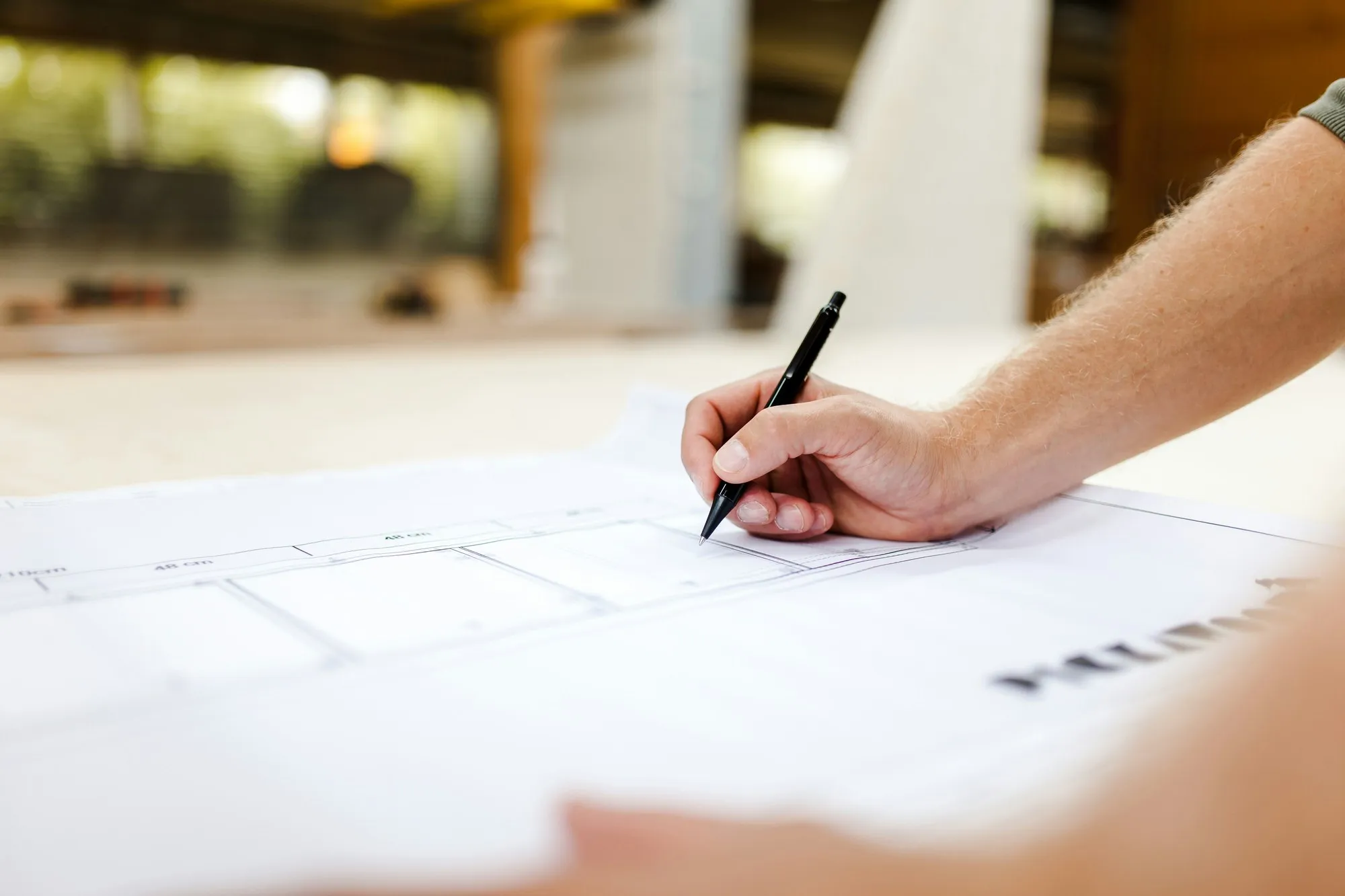 Hand with pen sketching on a large printed floor plan in daylight