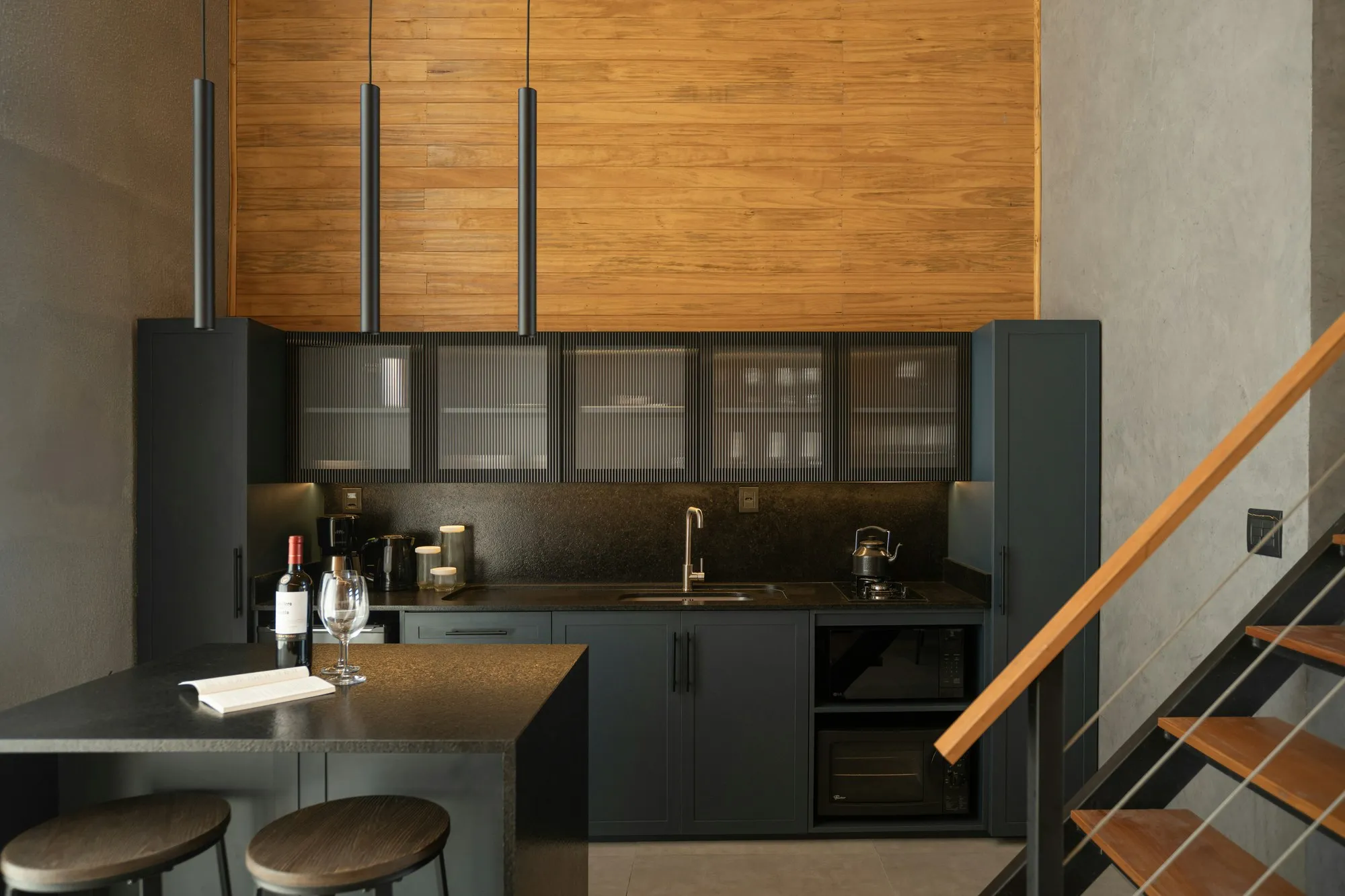 Finished loft apartment kitchen with island, concrete walls, timber cladding and steel staircase