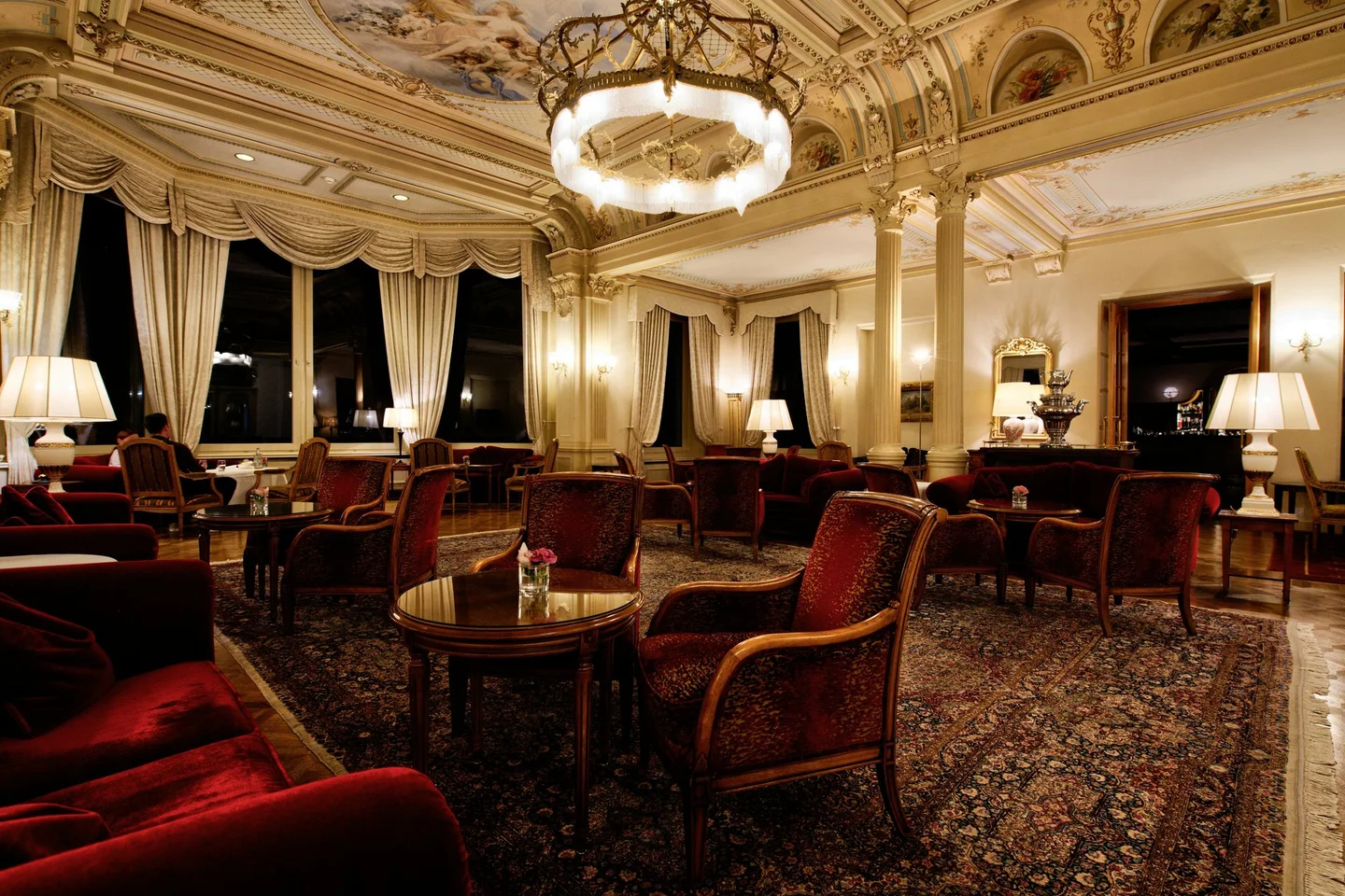 Grand period hotel salon with a painted ceiling, tall draped windows and formal seating