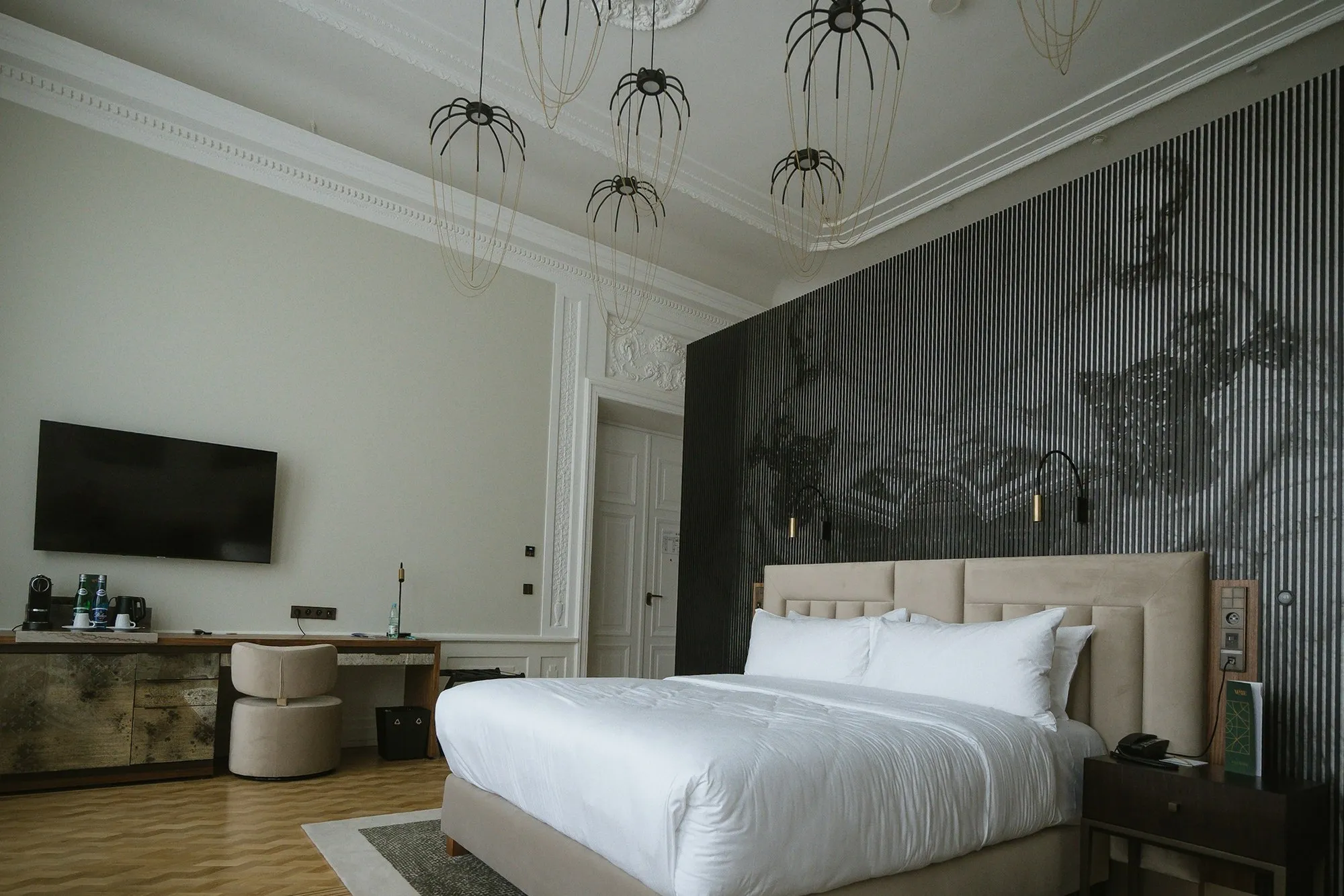 Hotel bedroom with a beige upholstered headboard, a black slatted feature wall and a cluster of pendant lights