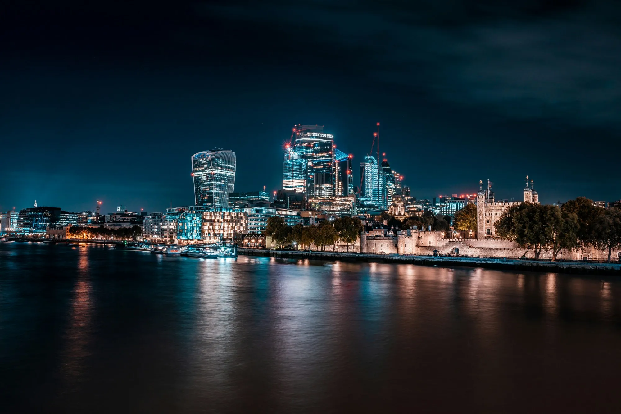 City of London towers and Tower of London across the Thames at night, long-exposure reflections