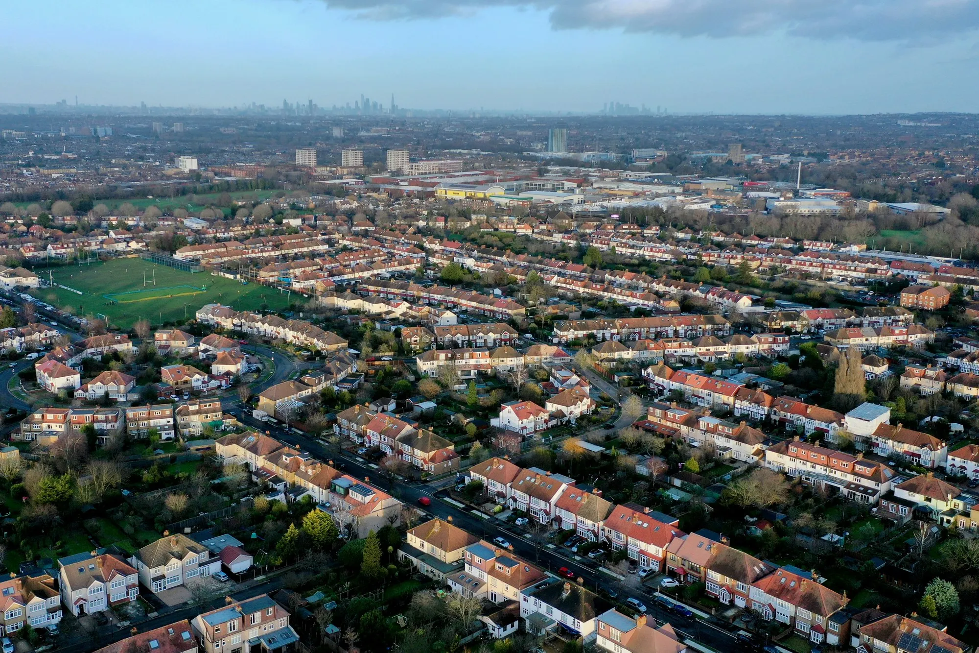 Elevated view over rows of London terraced houses and back gardens towards the distant City skyline, late light