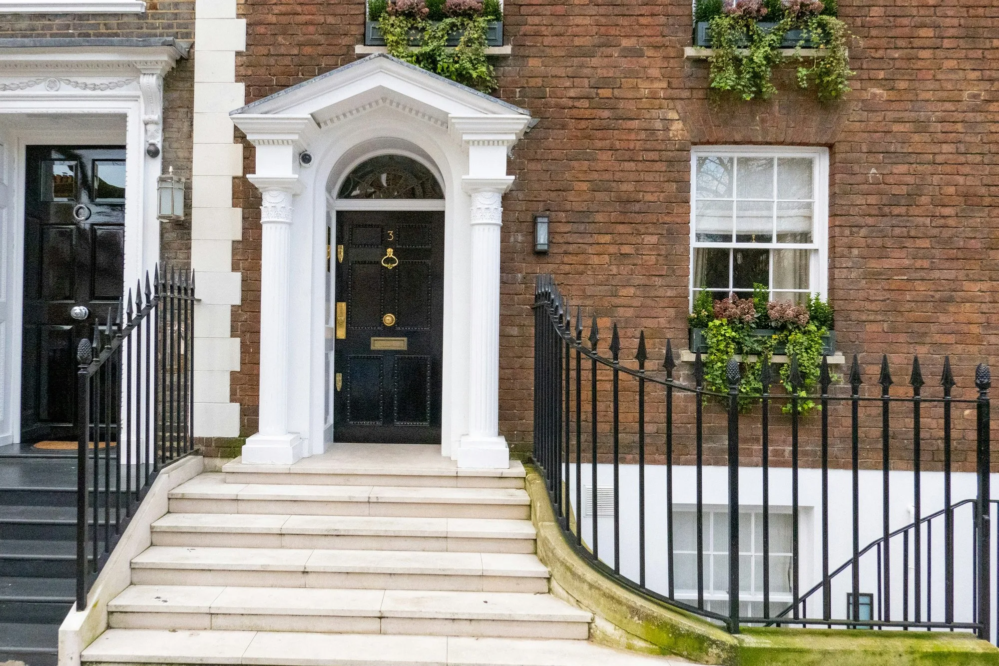 London brick townhouse entrance with white stone portico, black panelled door with brass fittings and black railings, daylight
