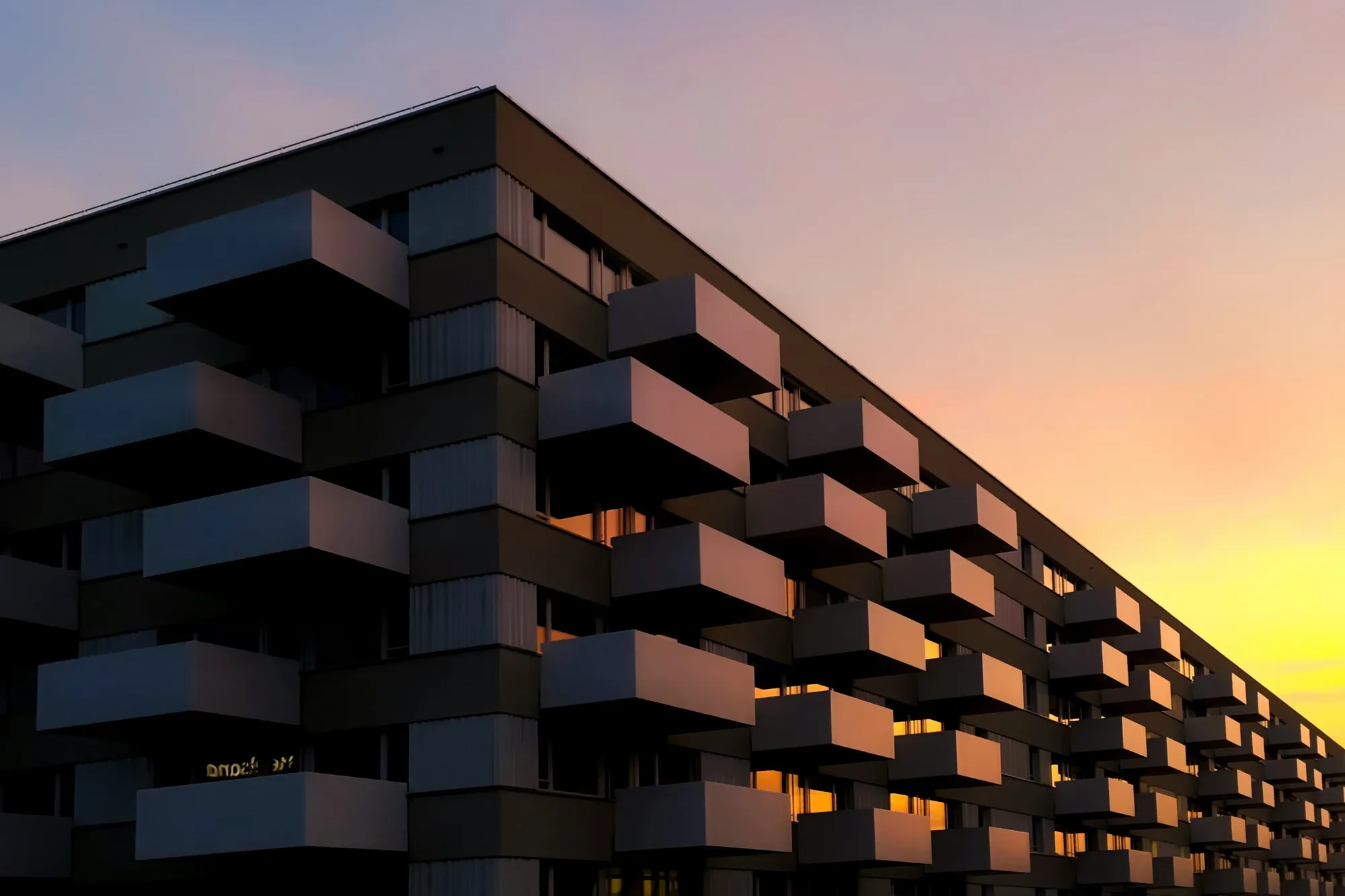 Contemporary apartment block with deep balconies at golden-hour sunset, warm light on the facade