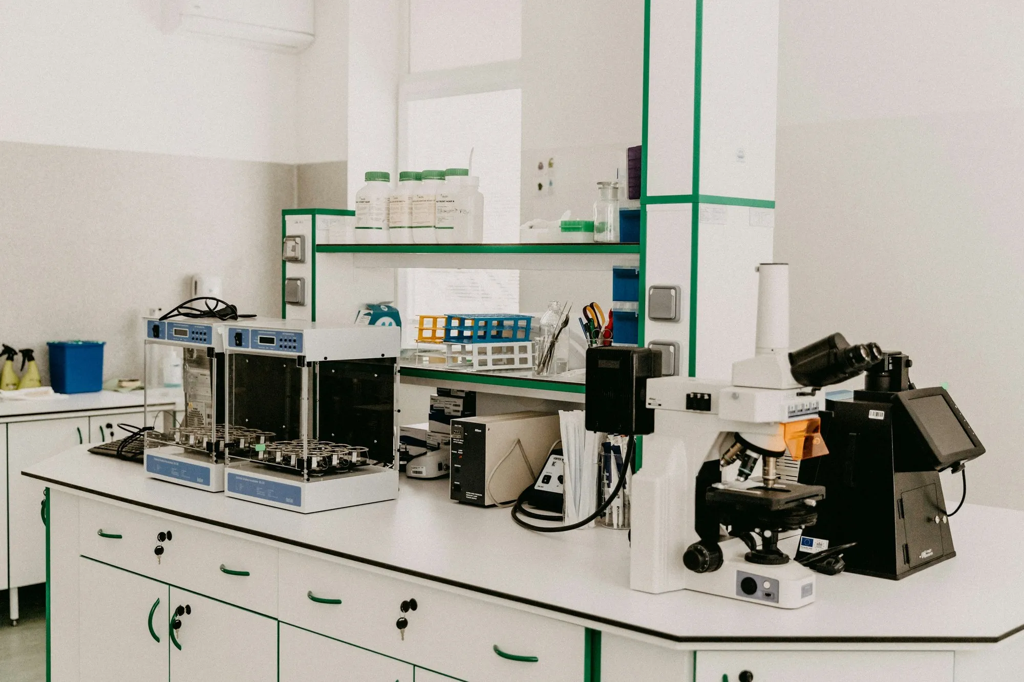 Lab bench with shelving, reagents and microscopes in a bright laboratory