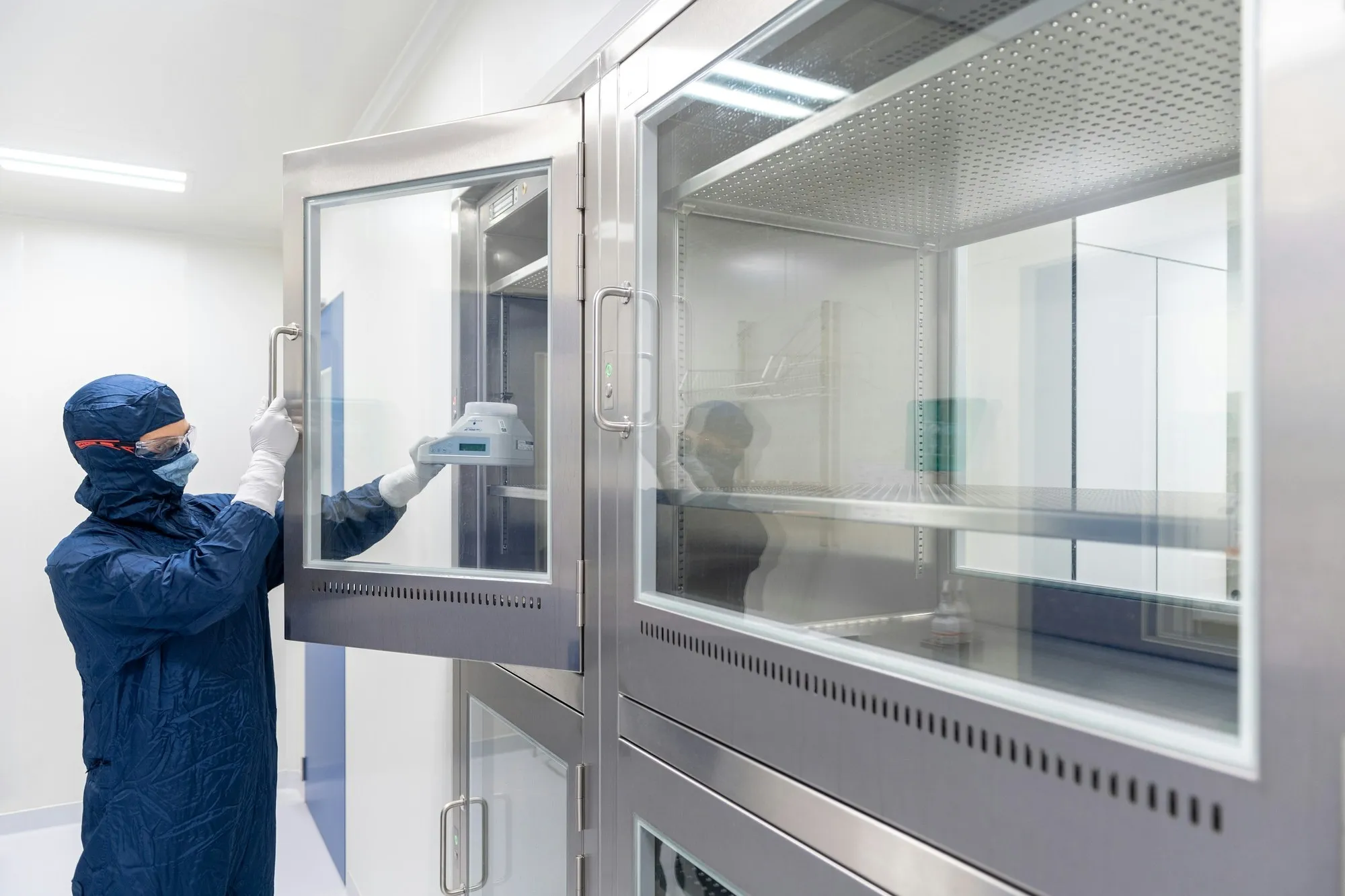 Technician in cleanroom suit opening a stainless steel glazed cabinet