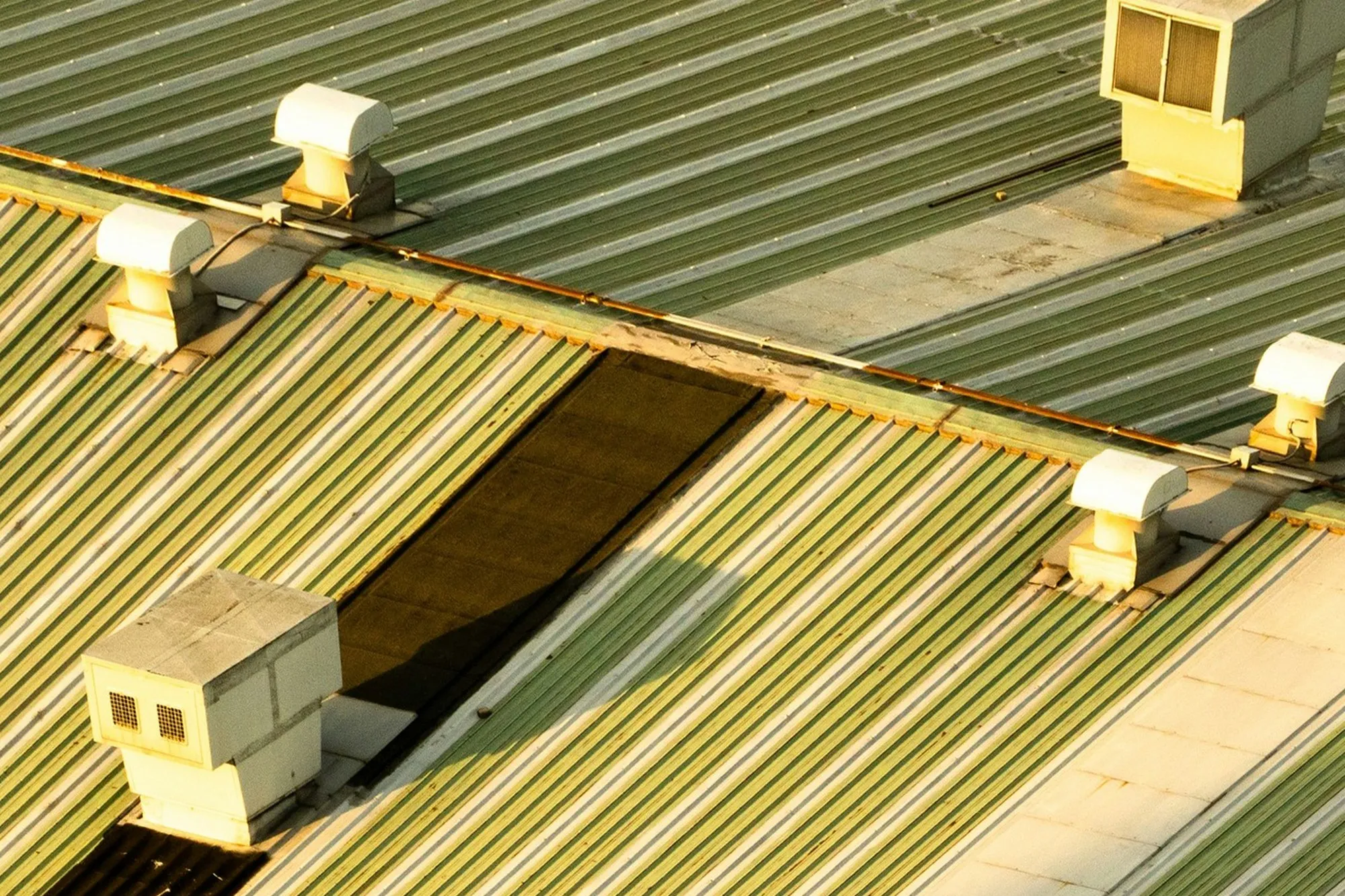 Rooftop ventilation units on a metal roof in warm low sun