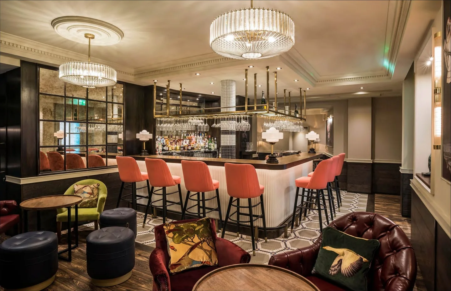Sloane Place bar in Chelsea: coral velvet bar stools at a fluted white counter, crystal chandelier and leather chesterfield seating