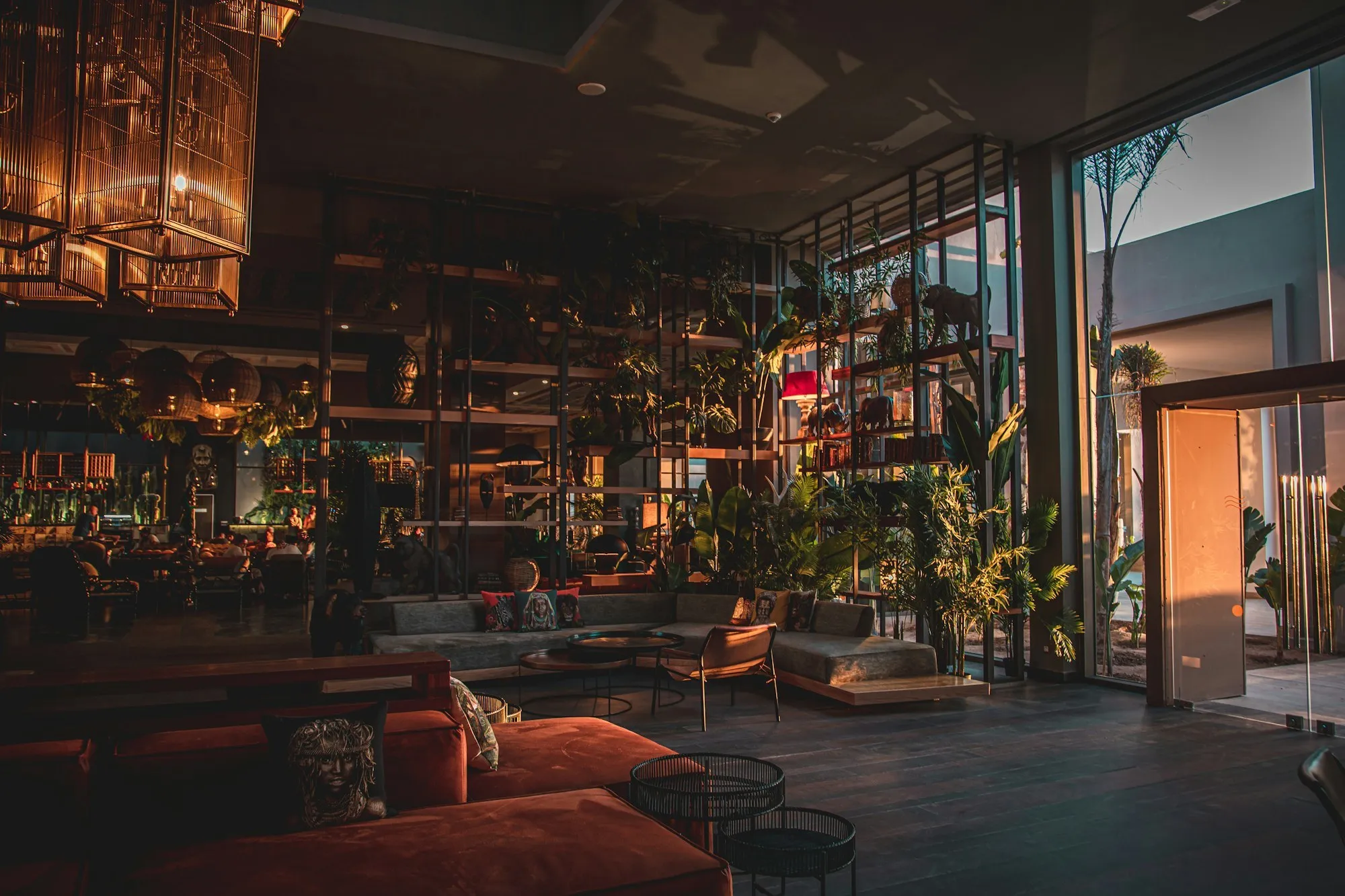 Dimly lit luxury lounge bar with red velvet chairs, a long back bar and brass pendant lights