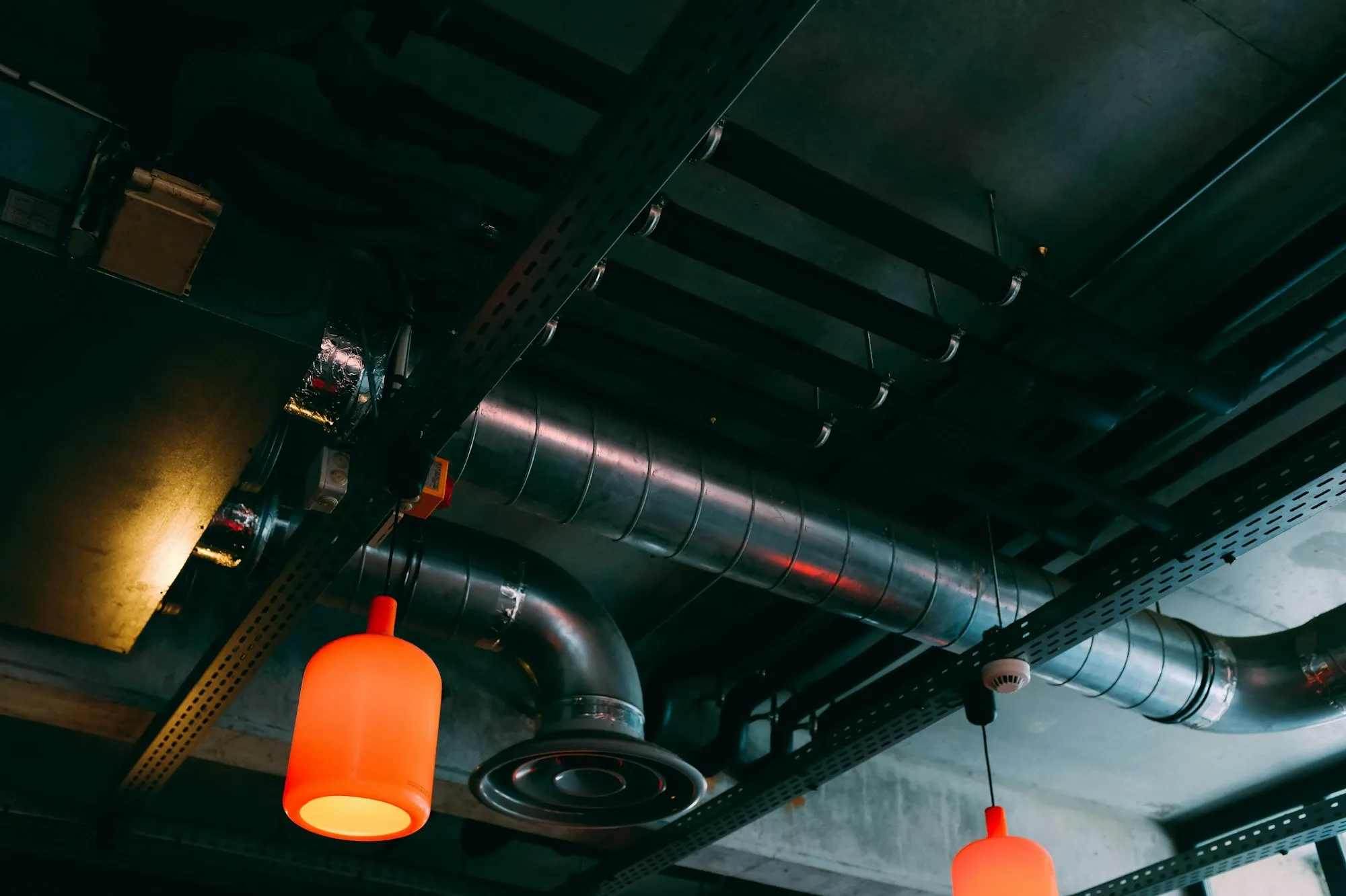 Restaurant interior with exposed ventilation ductwork, air handling and pendant lighting above the tables