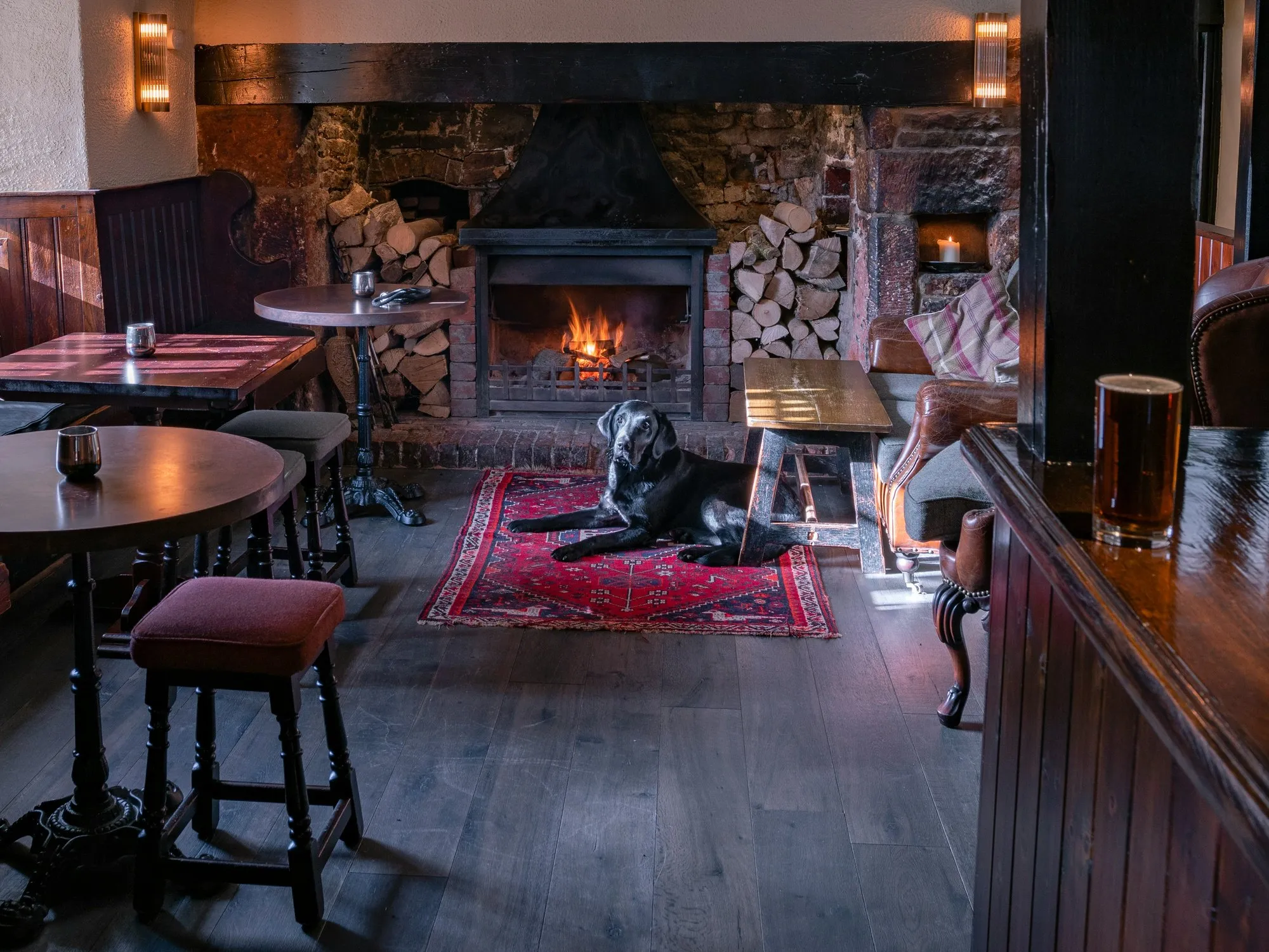 Traditional pub interior with a lit open fire, timber bar, stools and a red rug
