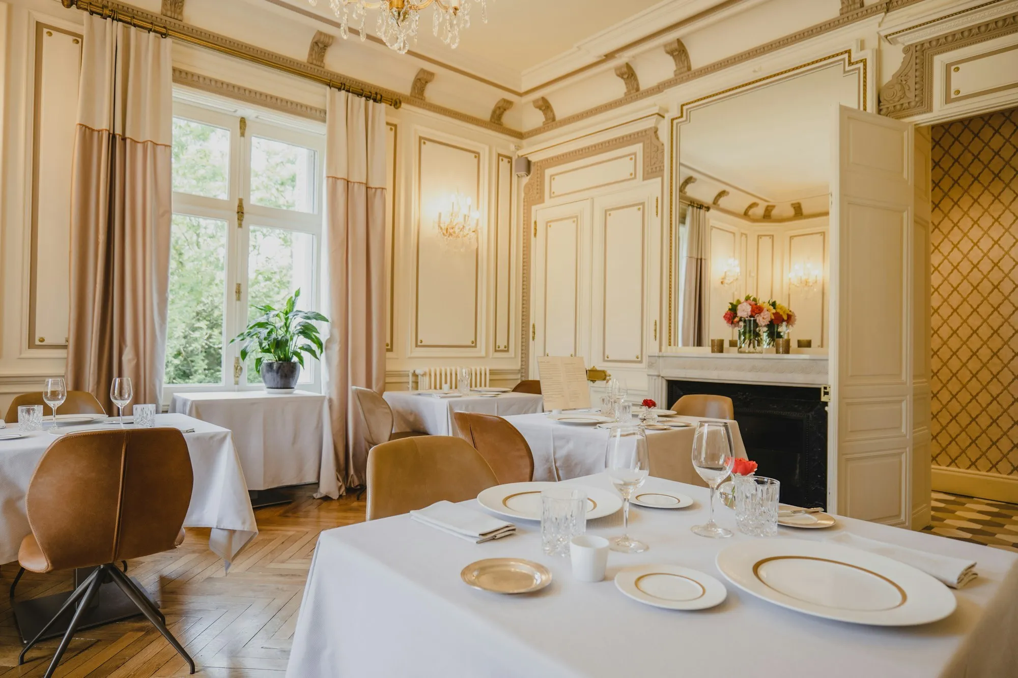 Period dining salon with white tablecloths, panelled walls, a marble fireplace and tall windows