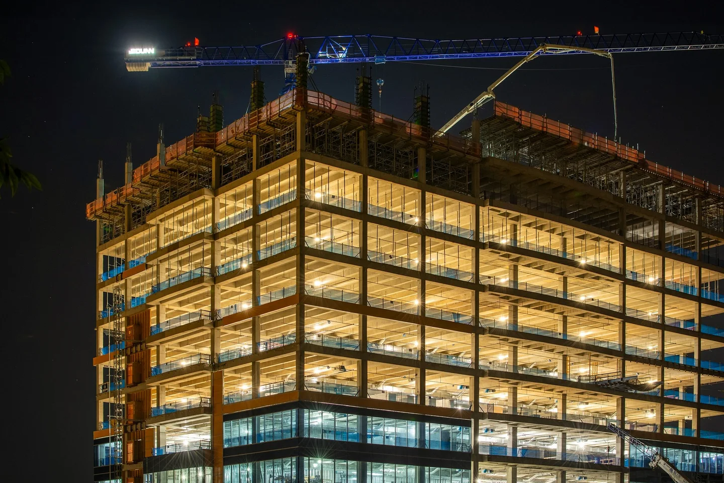Lit office frame under construction at night beside a tower crane