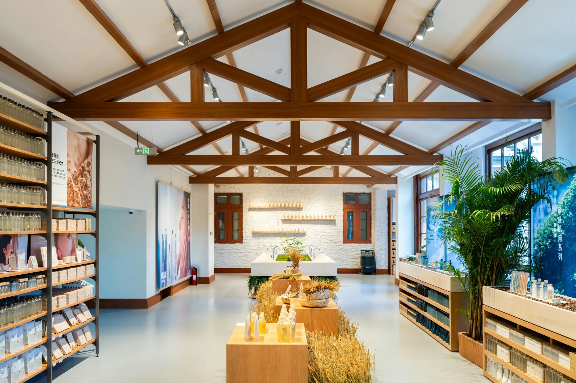 Bright retail floor under exposed timber roof trusses with timber shelving and display plinths