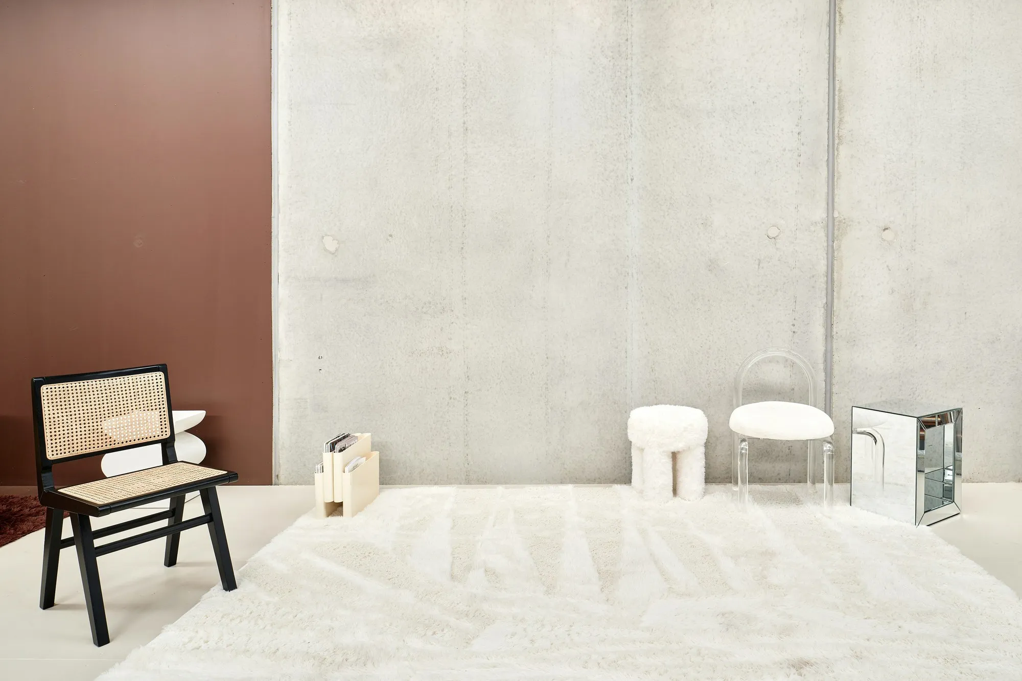 Minimal furniture showroom with cane chair, stools and white rug against a concrete wall