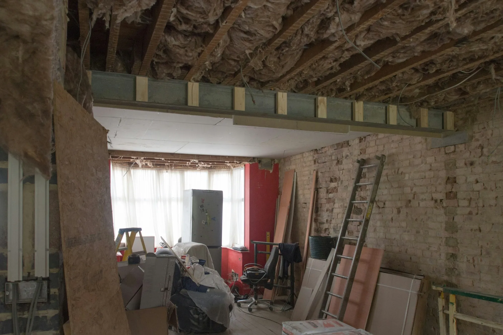 Stripped-out ground-floor unit with exposed joists and insulation, steel beam, bare brick wall and bay window