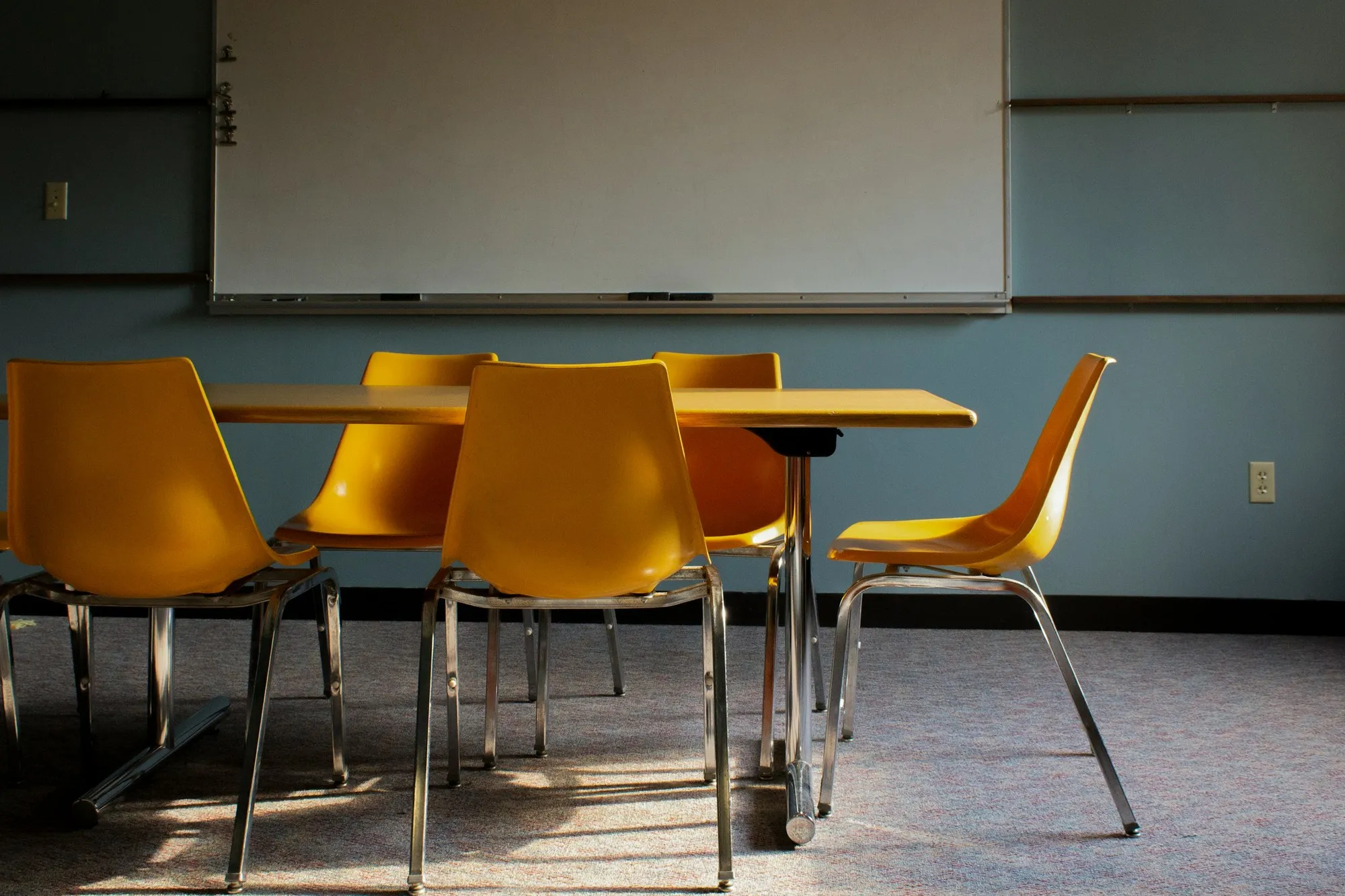 Empty classroom with table, orange chairs and wall-mounted whiteboard