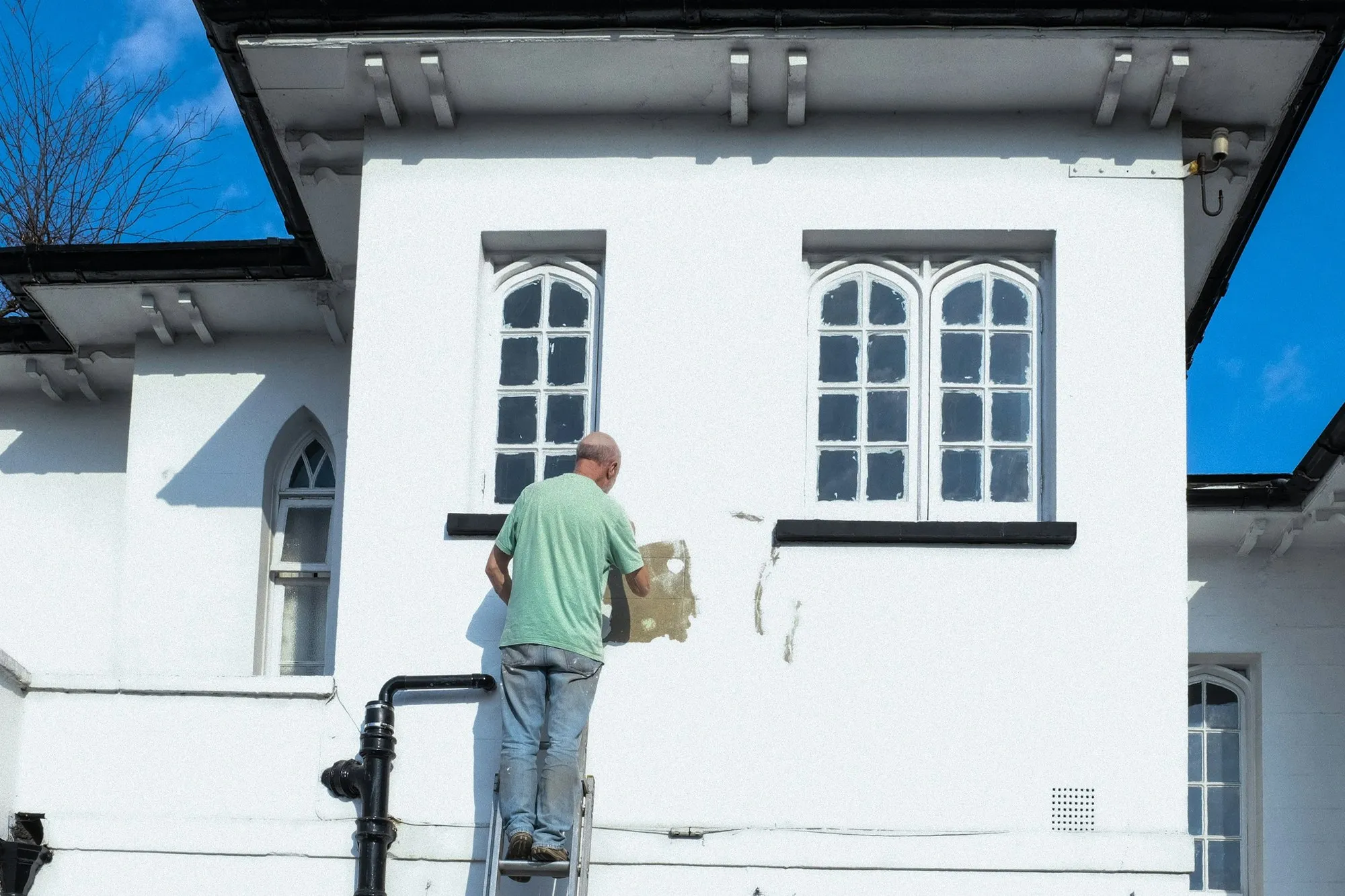Painter on a ladder redecorating a white rendered building facade