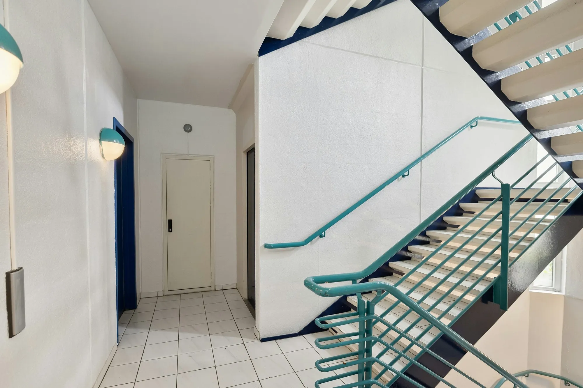 White communal stairwell with teal handrail and stair landing