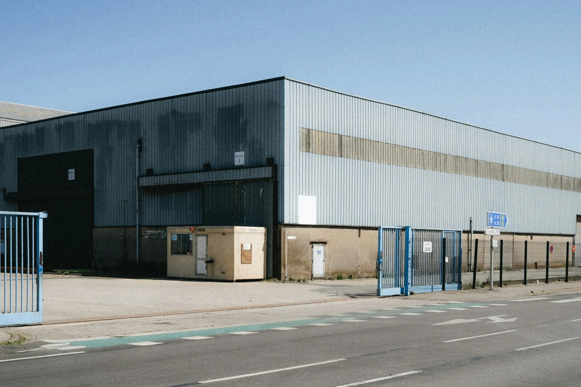 Large steel-clad warehouse building behind a blue site gate