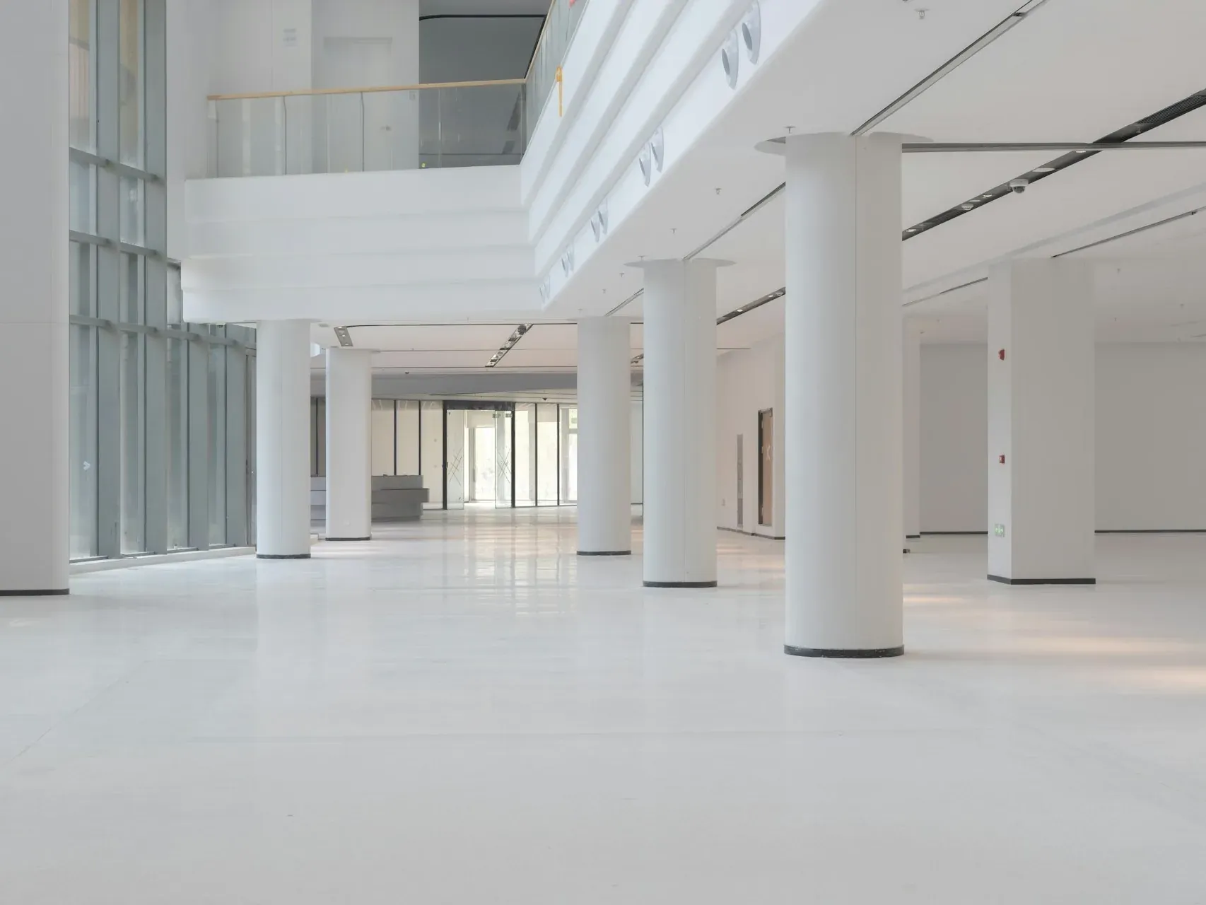 Large white commercial building interior with tall glazing, round columns and a mezzanine gallery