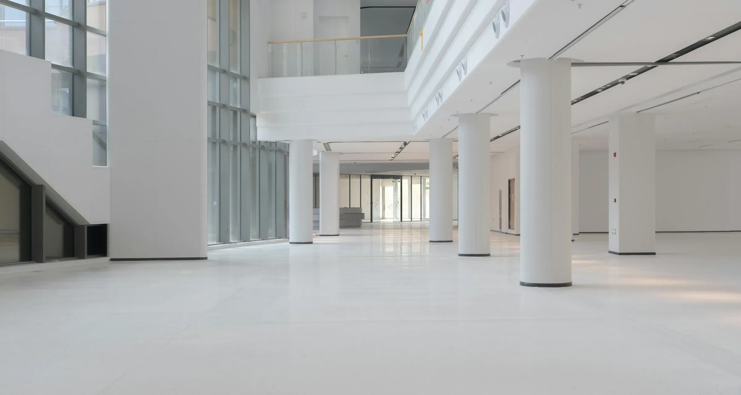 Empty white commercial floor with round columns, full-height glazing and a mezzanine, before any fit-out