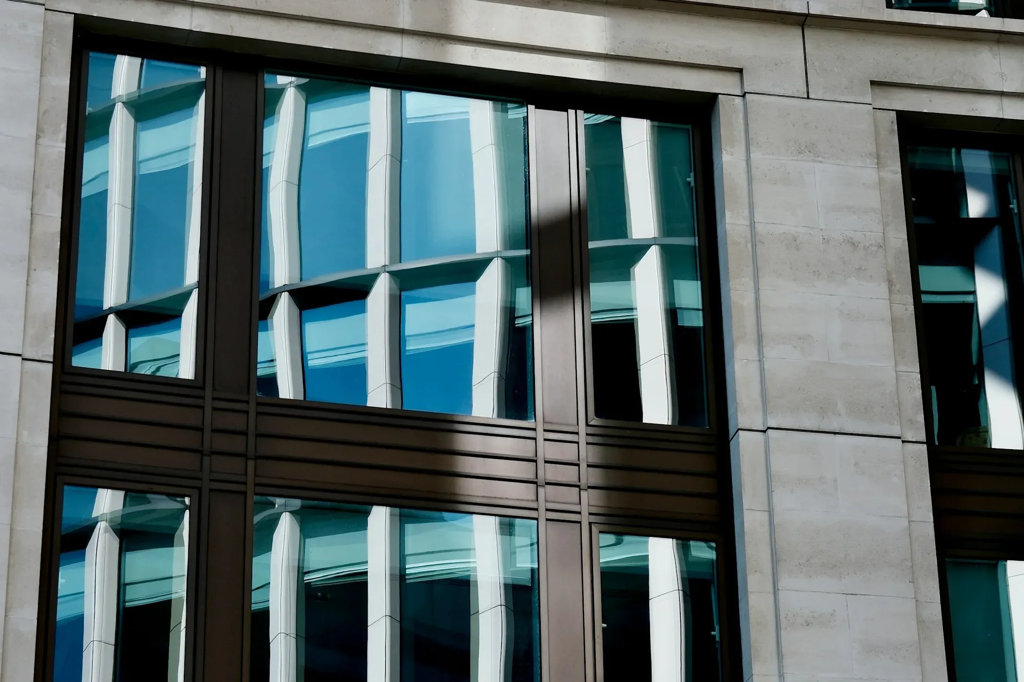 Portland stone office building in the City of London with bronze-framed windows reflecting the buildings opposite