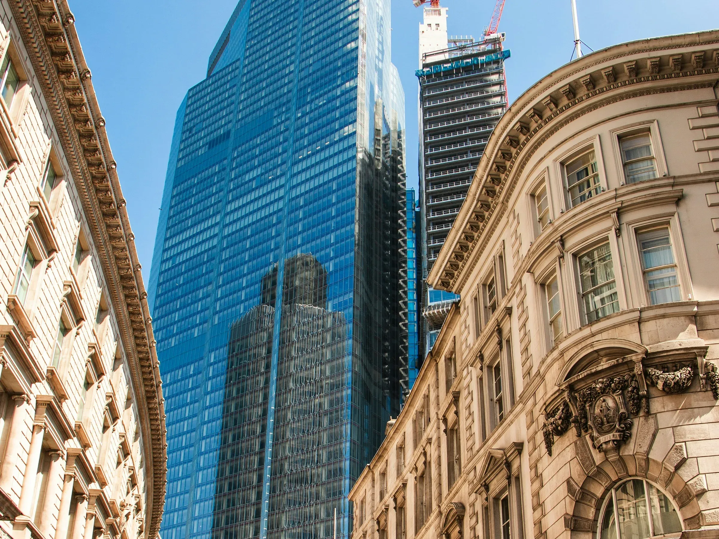 Glass office tower rising behind stone-fronted commercial buildings on a sunny City of London street