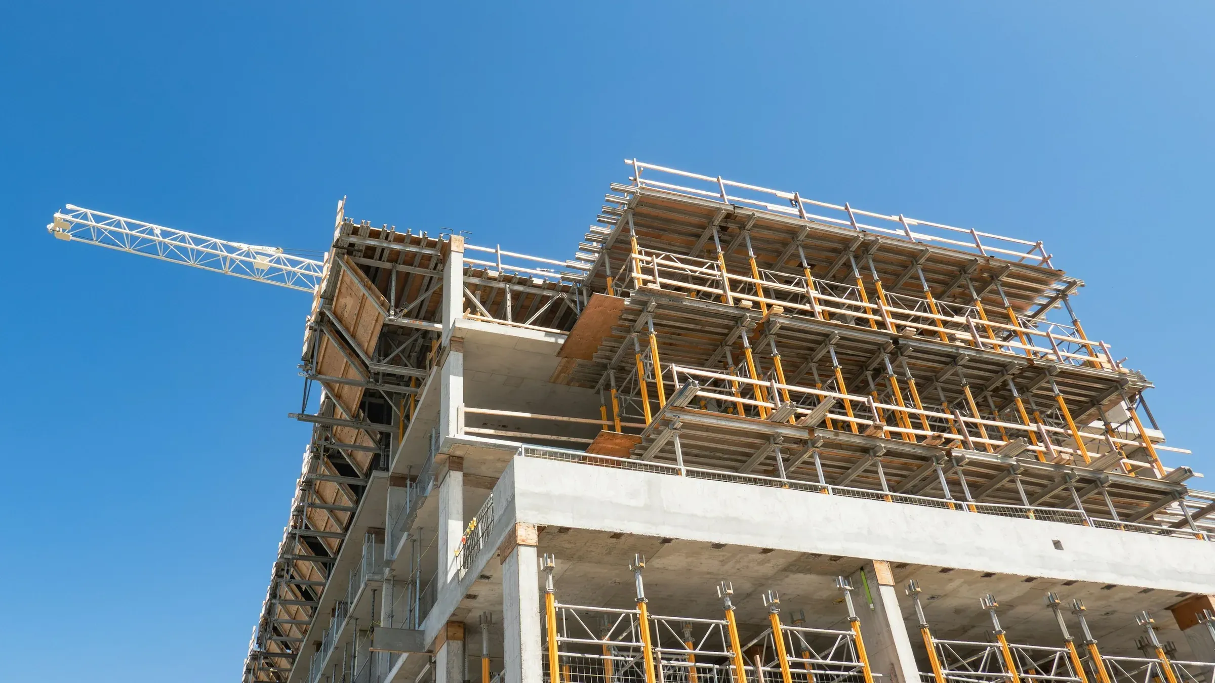 Concrete frame of a mid-rise building under construction with a tower crane against a blue sky