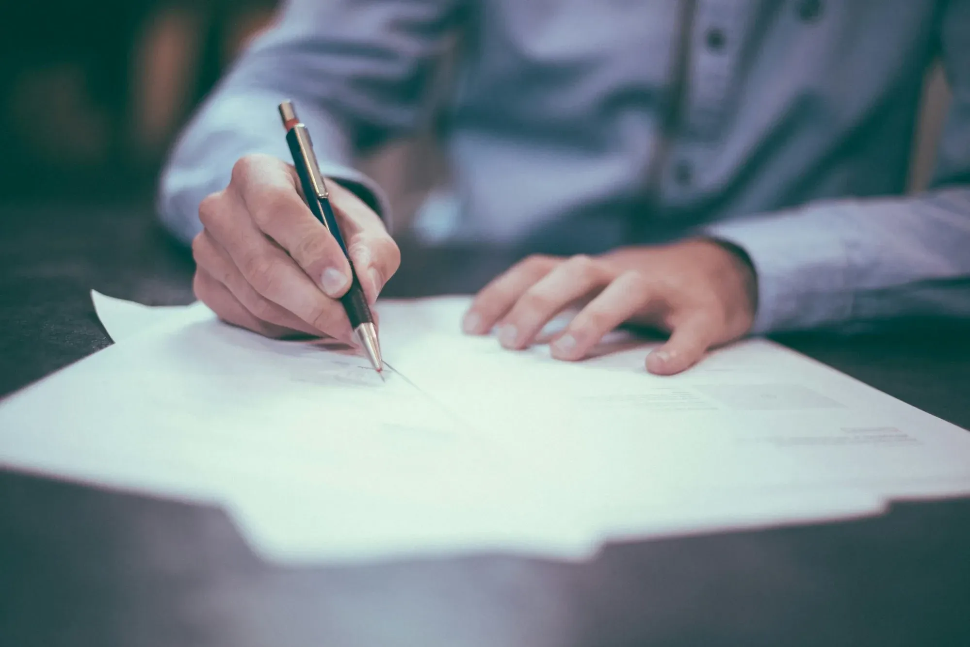 Hand signing a document with a pen on a desk