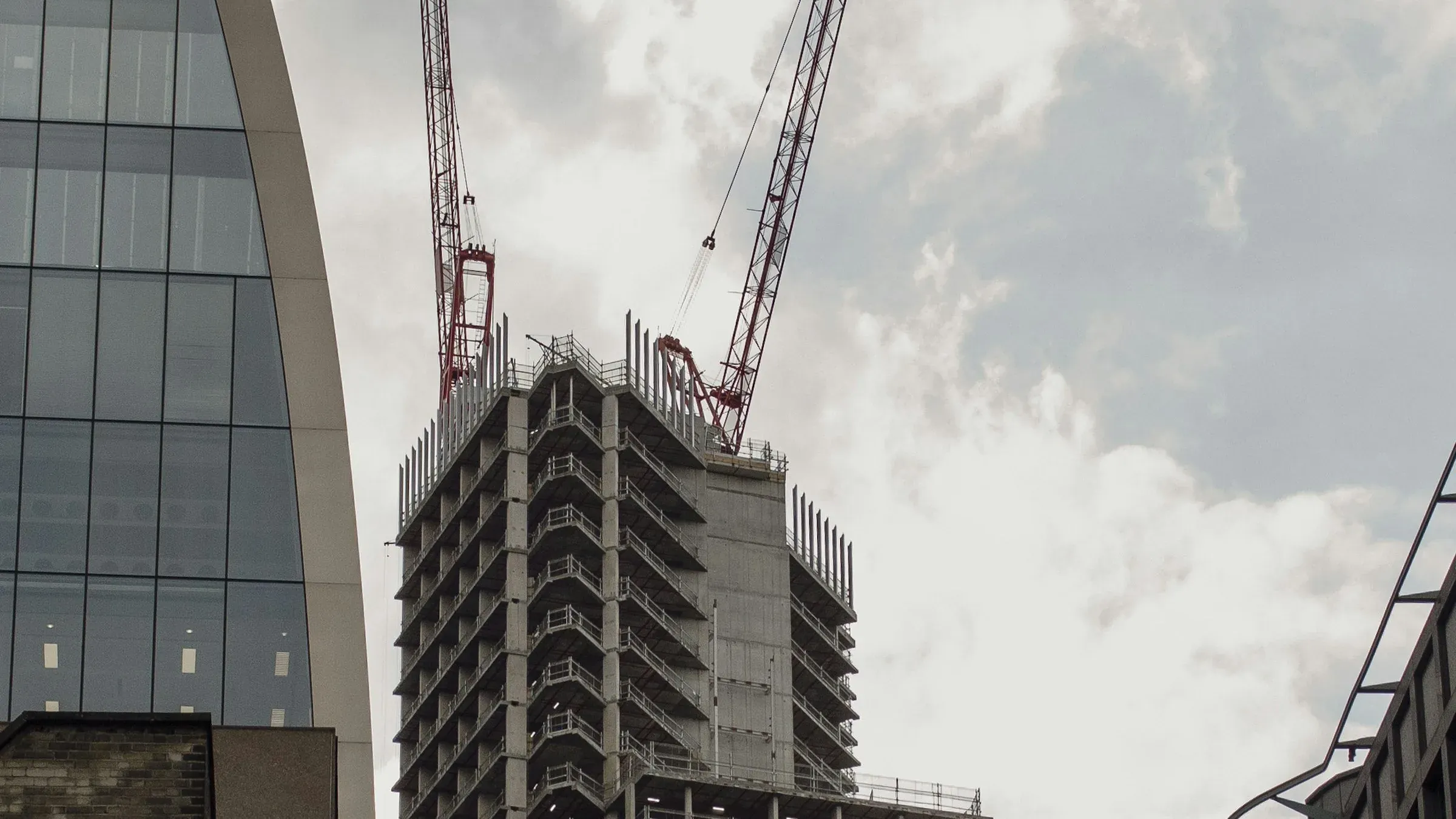 Concrete frame of a commercial tower under construction in the City of London with two tower cranes above it