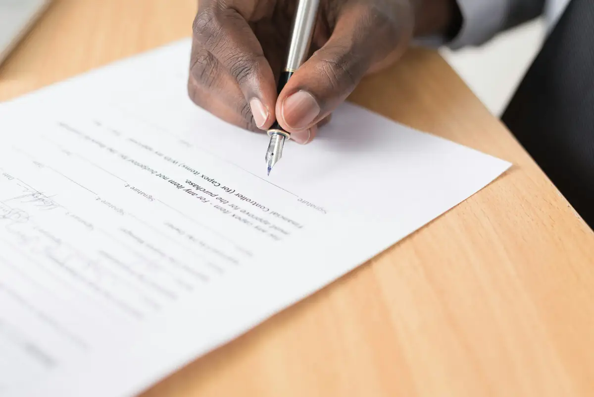Hand signing a printed document with a fountain pen on a wooden desk