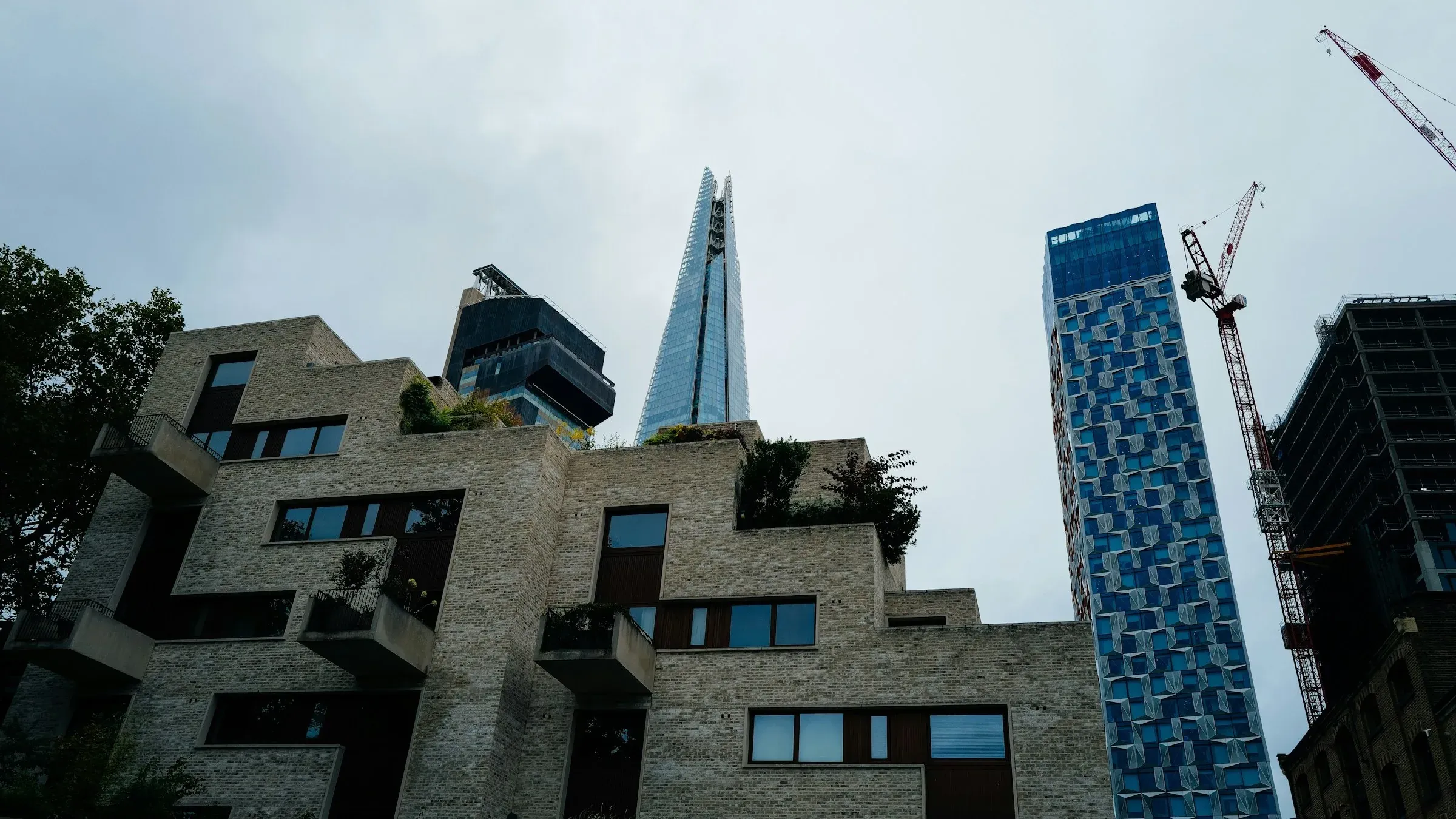 London towers beside the Shard with construction cranes against a cloudy sky
