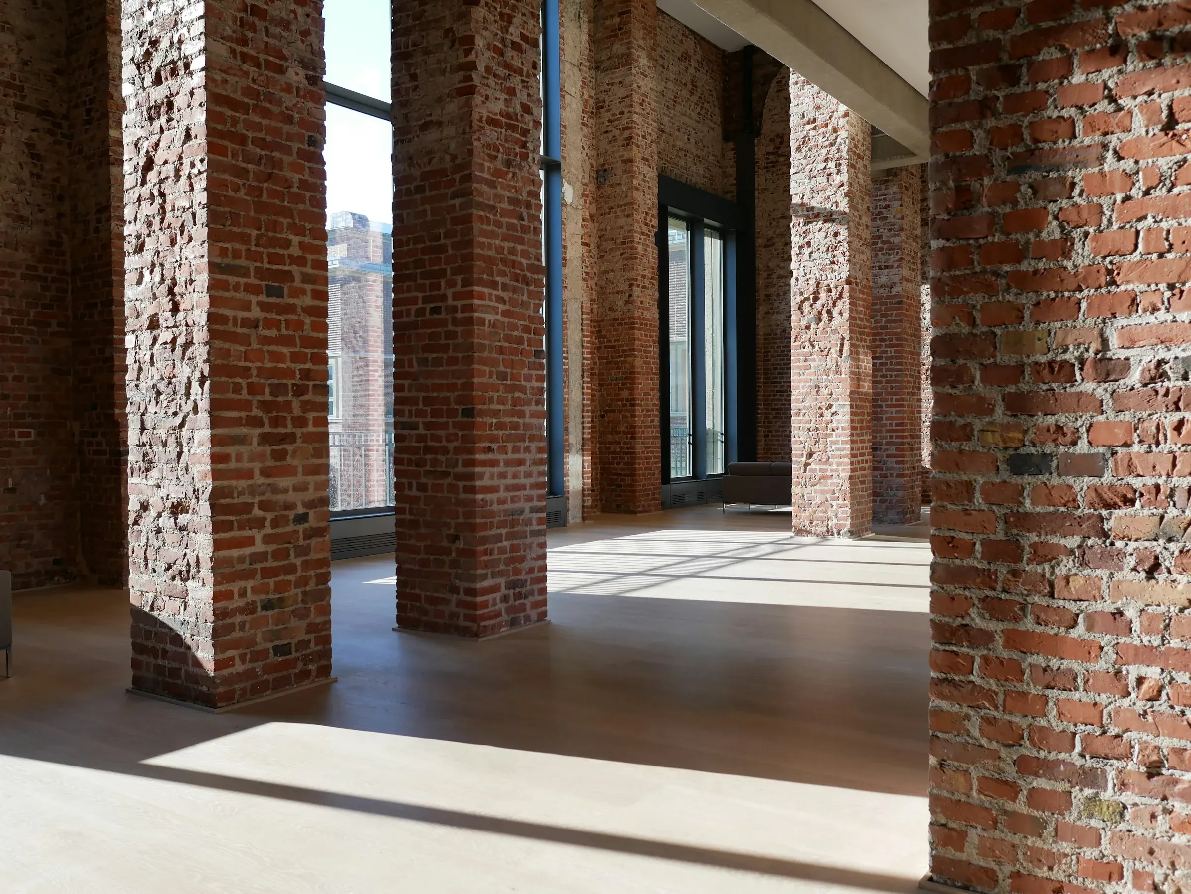 Stripped floor of a period brick building with exposed brick columns, tall windows and a new timber floor