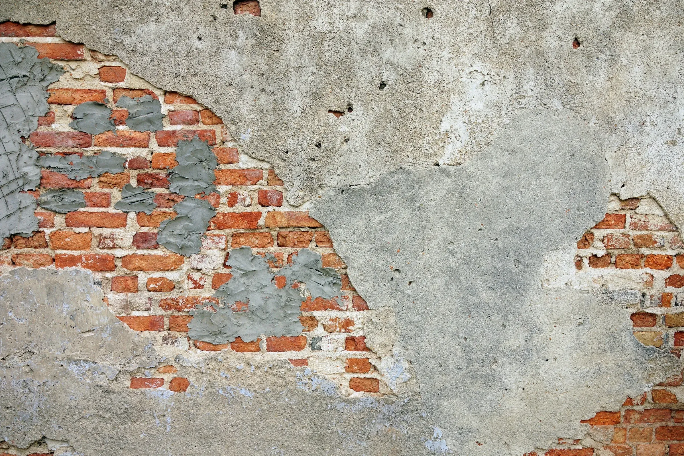 Old brick wall with patches of fresh mortar and plaster where it is being repaired