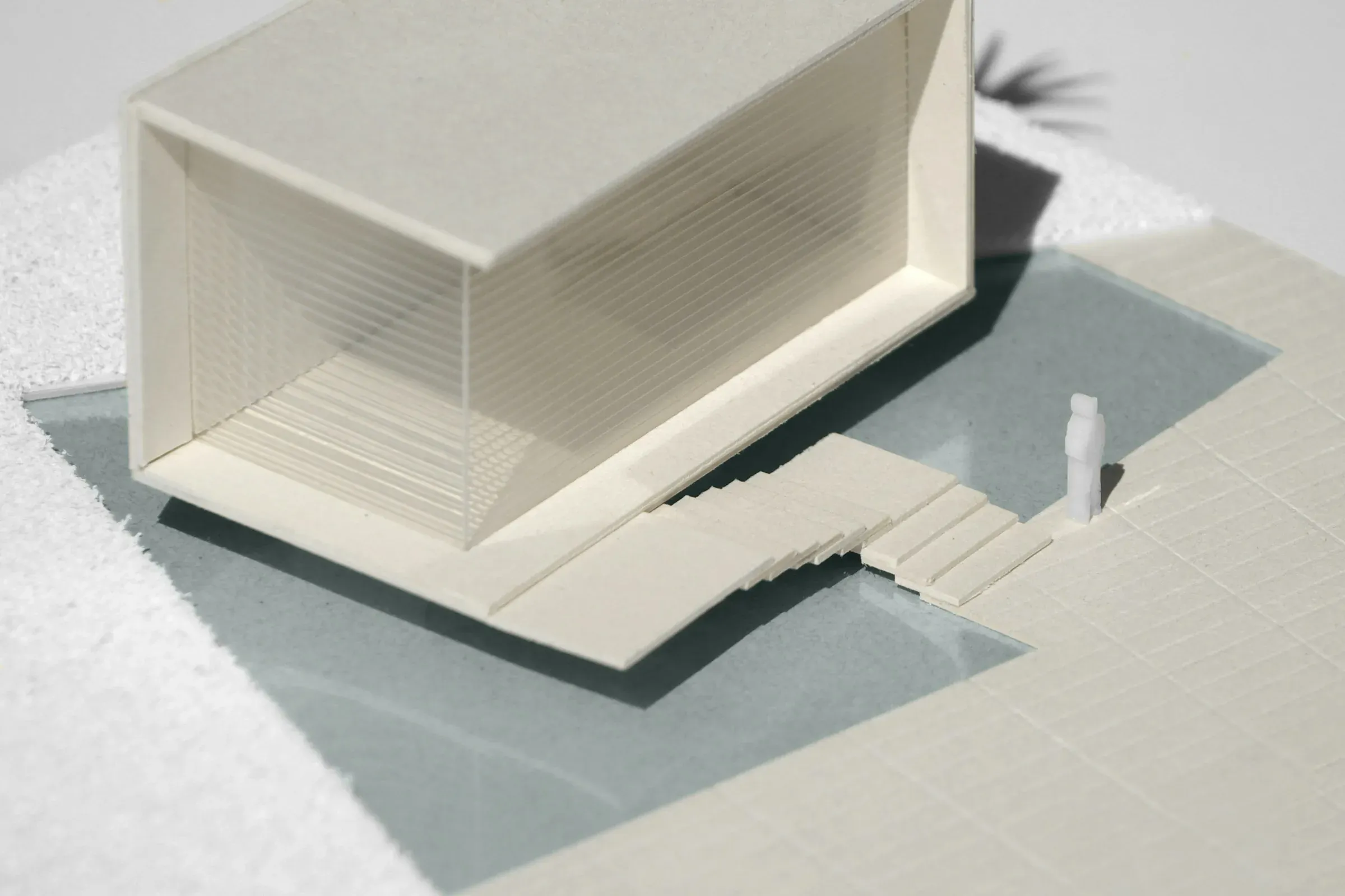 White architectural scale model of a house with glazed walls and steps, on a table