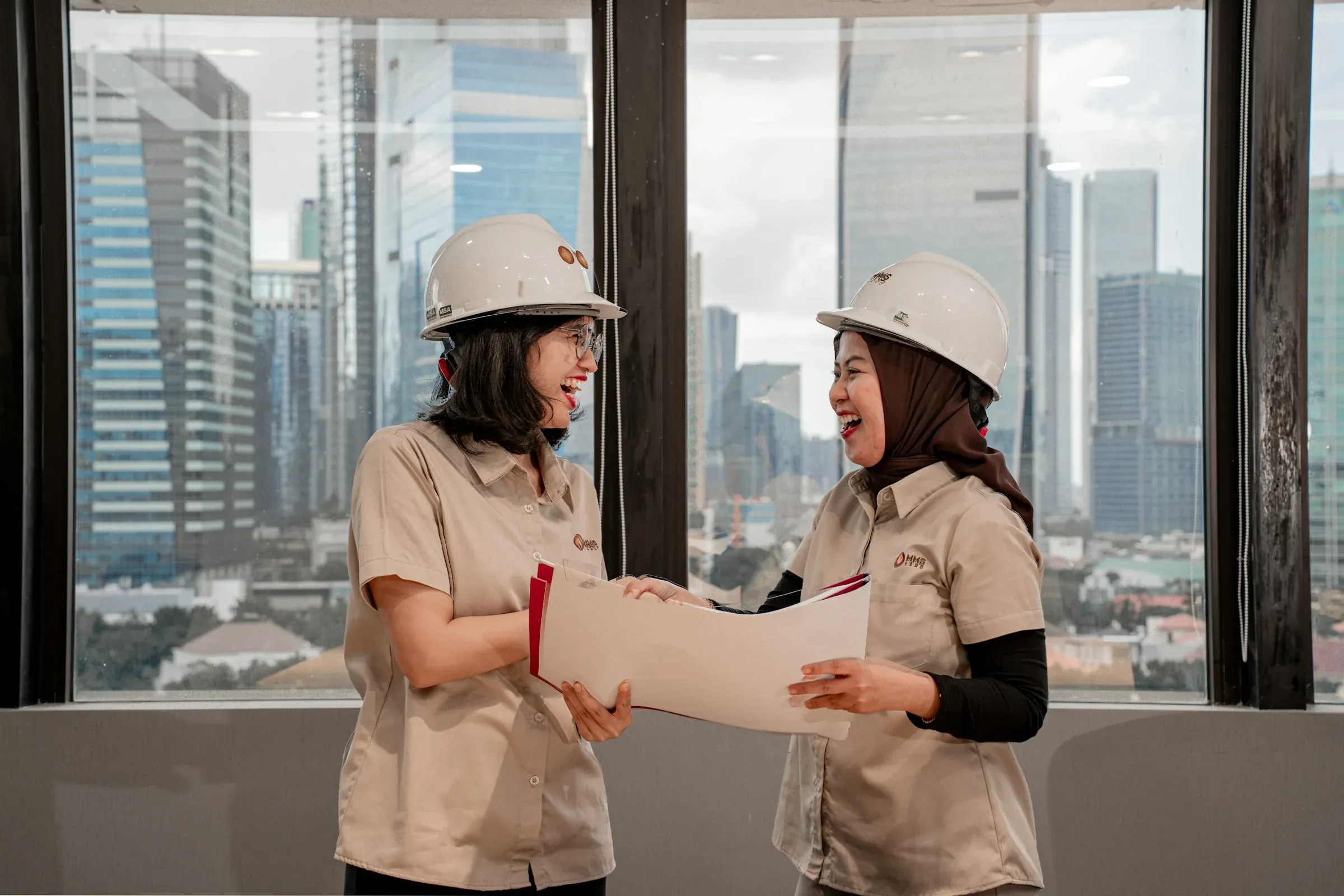 Two people in hard hats reviewing a set of drawings by an office window