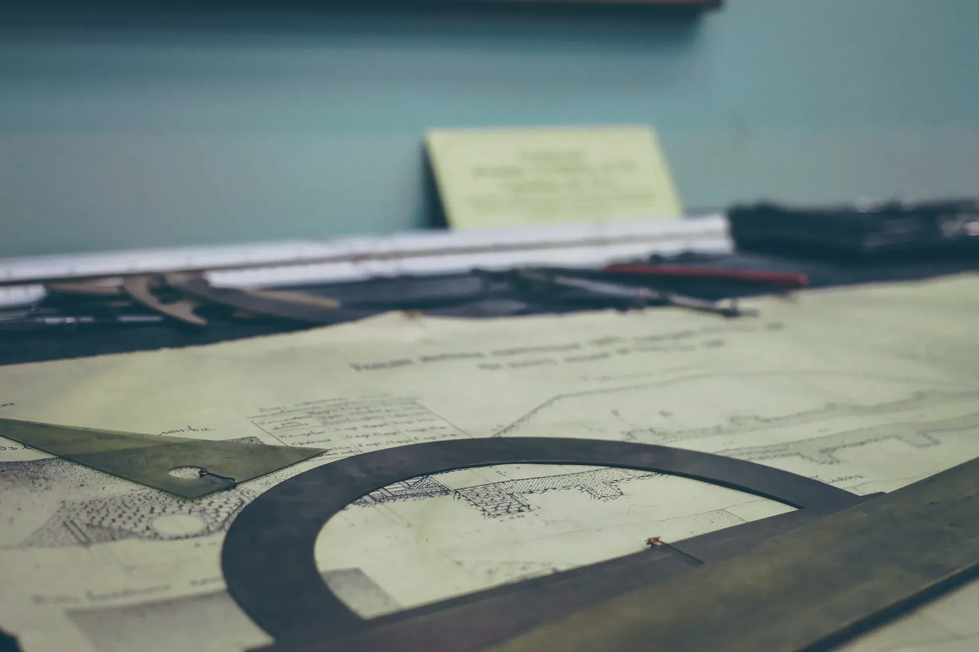 Printed construction drawings on a desk with drafting tools and a protractor
