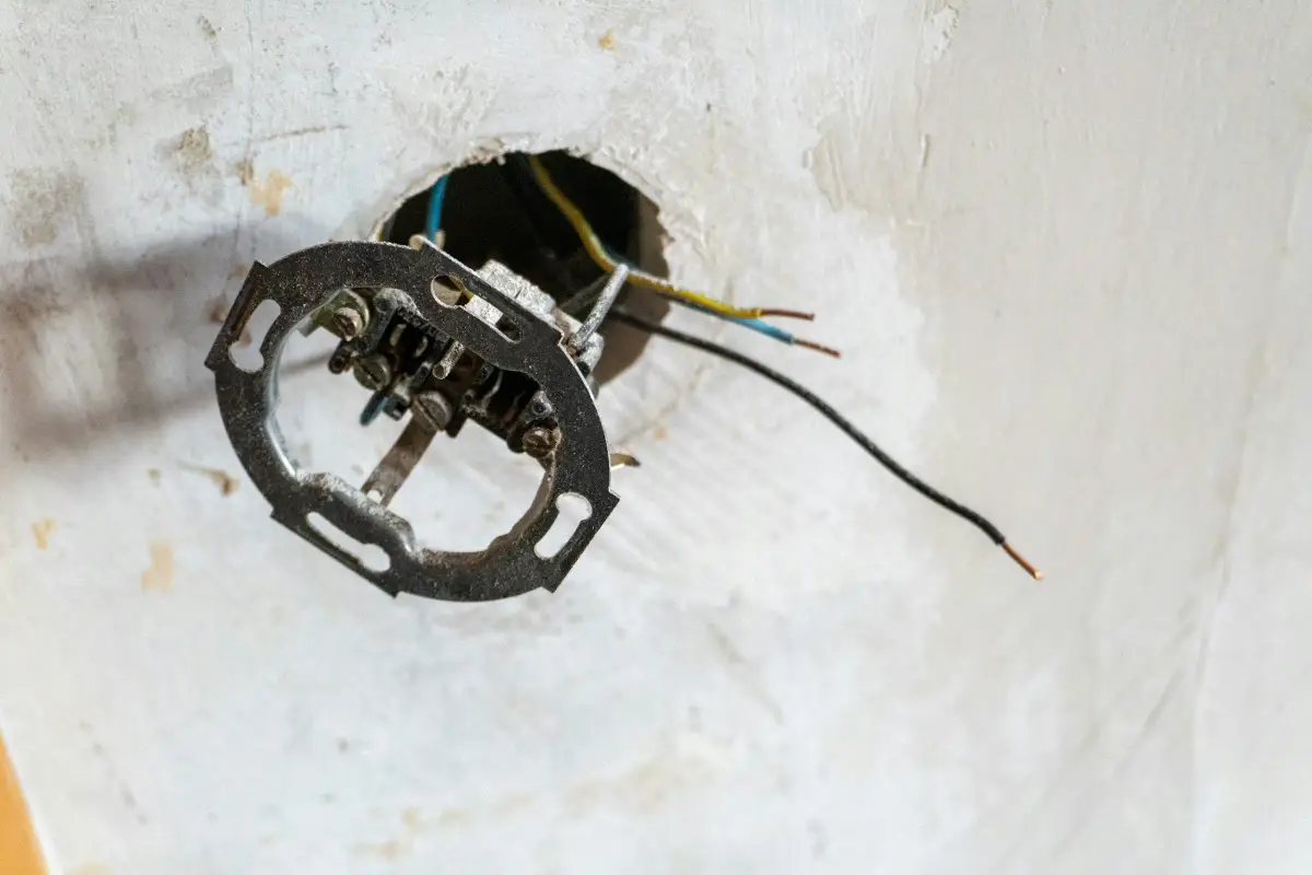 Exposed electrical wires and a socket mounting box in a rough plaster wall