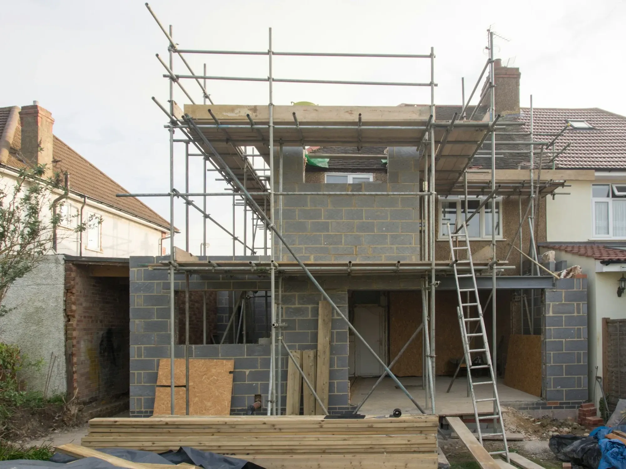 Rear house extension in blockwork under scaffolding, with timber and a ladder on site