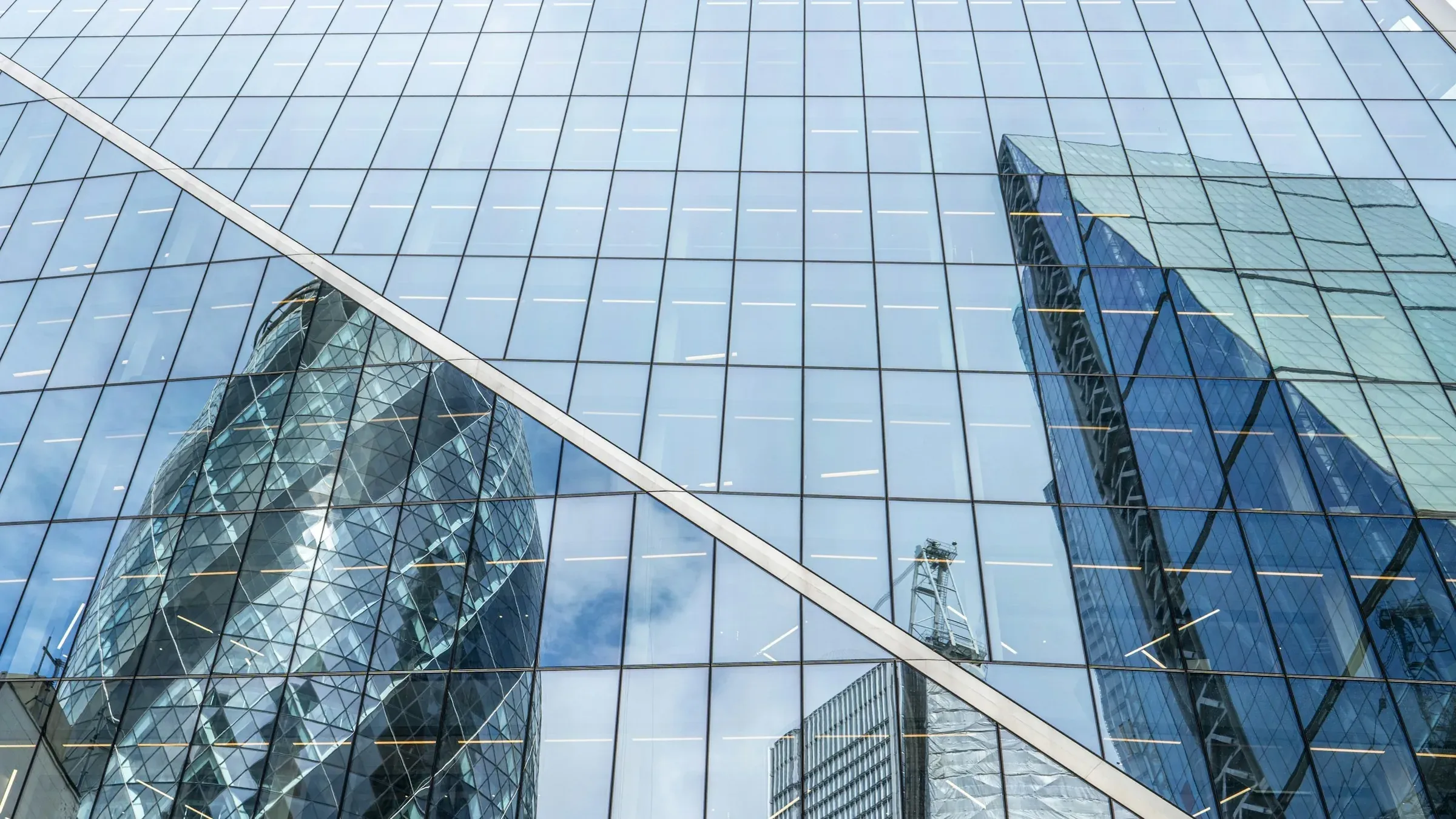 Close-up of a London glass office facade with a grid of mullions and transoms reflecting neighbouring towers