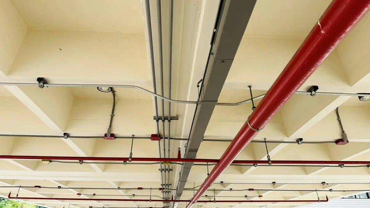 Concrete soffit with sprinkler pipework, steel conduits and trunking running across a ceiling
