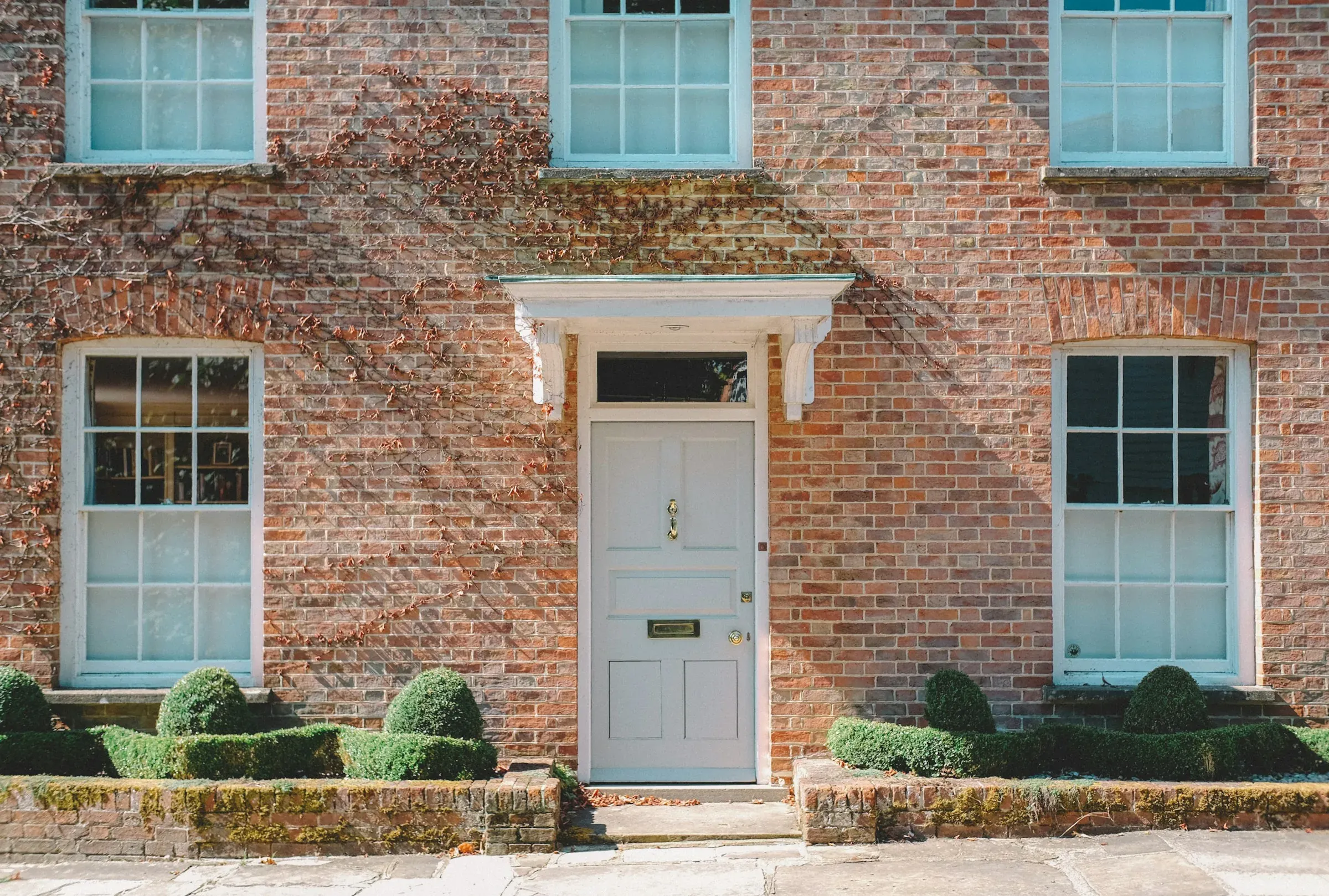 Georgian brick house front with a pale grey panelled door, sash windows and clipped box hedges