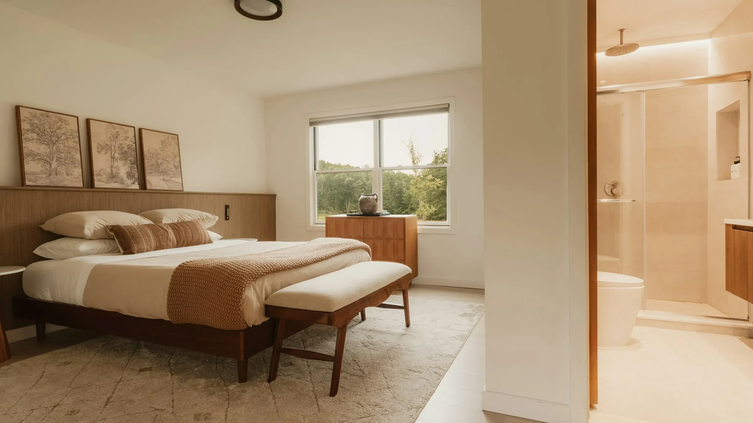 Hotel bedroom with a timber bed, bench and window onto trees, and a tiled en-suite shower beside it