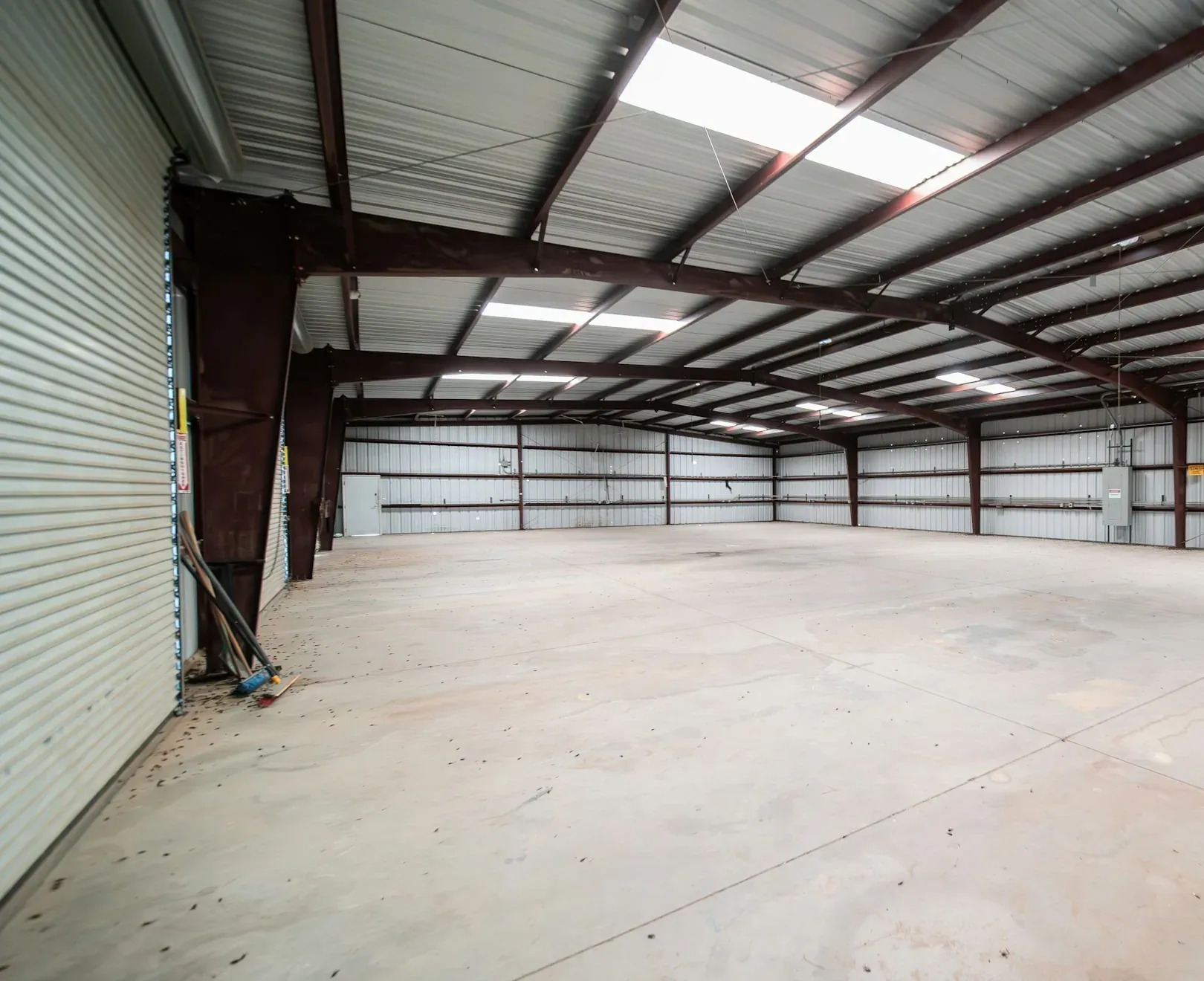 Empty steel-framed industrial unit with roller shutter doors, roof lights and a bare concrete floor